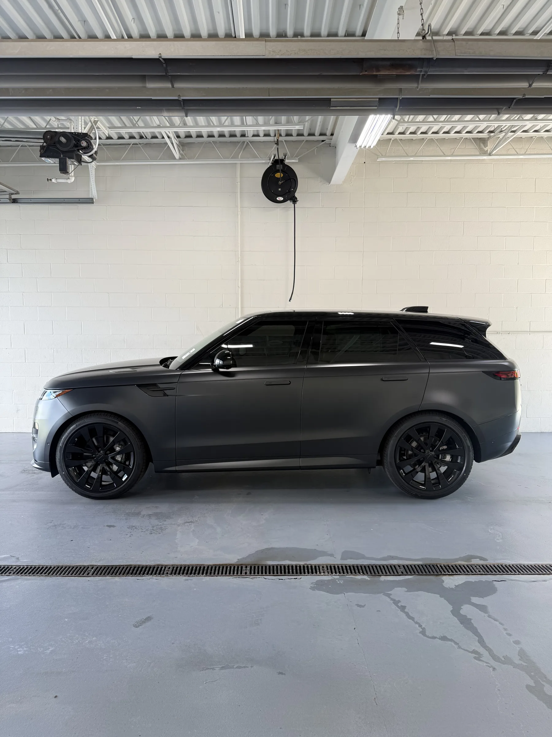 A black Range Rover Sport with tinted windows parked in a bright shop bay with white block walls and industrial ceiling.