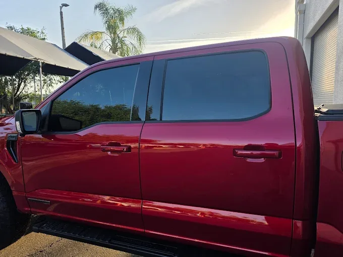 A red pickup truck with dark window tint applied to the cab windows, parked in a service lot.