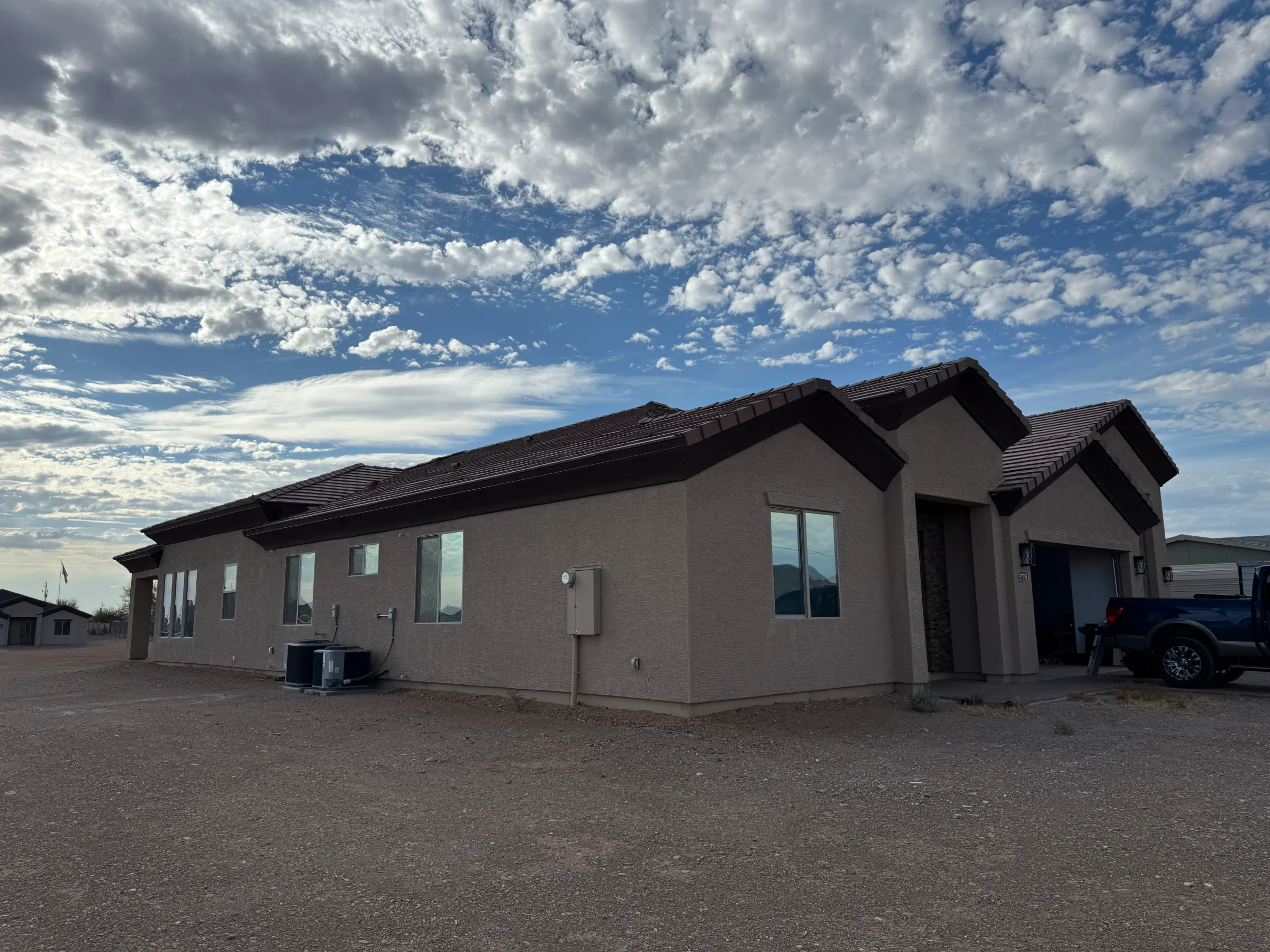 A tan and gray residential home with tinted windows under a blue sky with white clouds in Cave Creek, Arizona.