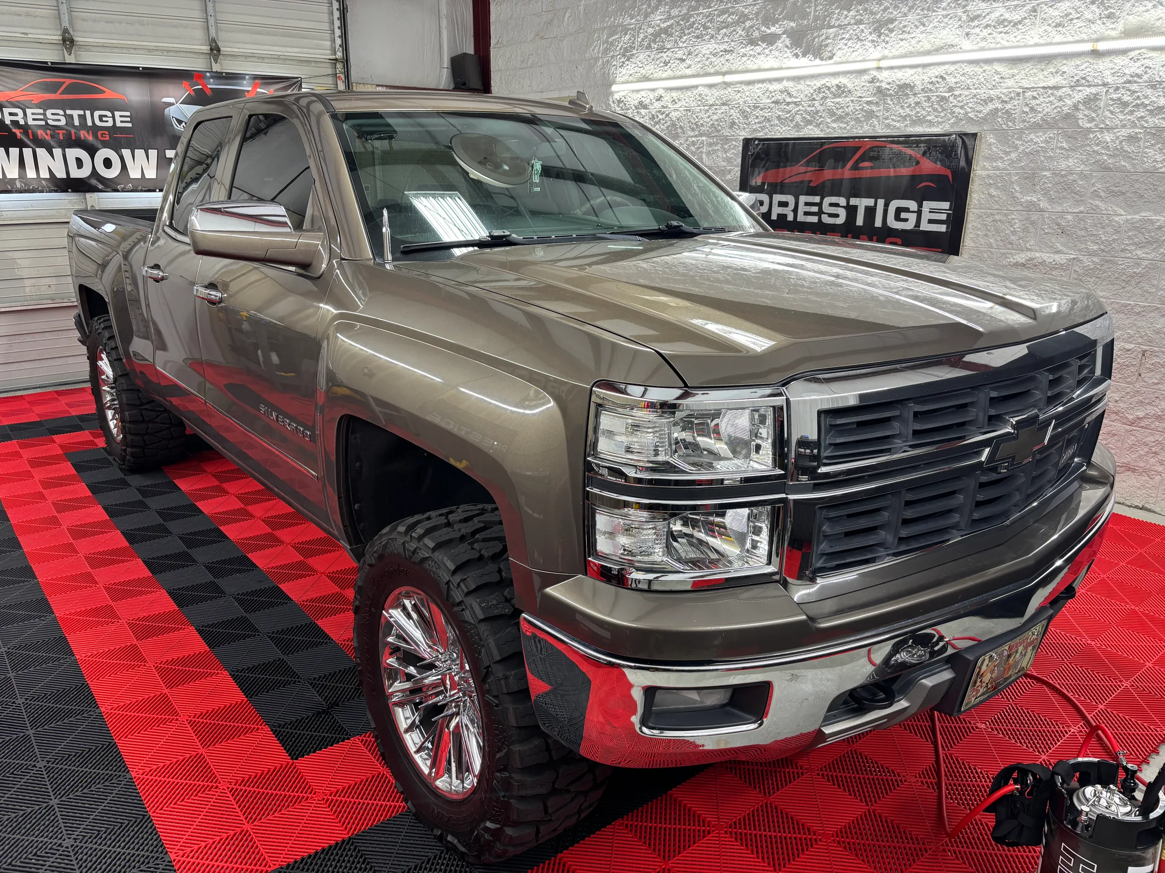 A tan and red two-tone Chevrolet Silverado pickup truck with tinted windows displayed in a showroom with Prestige Tinting branding visible.