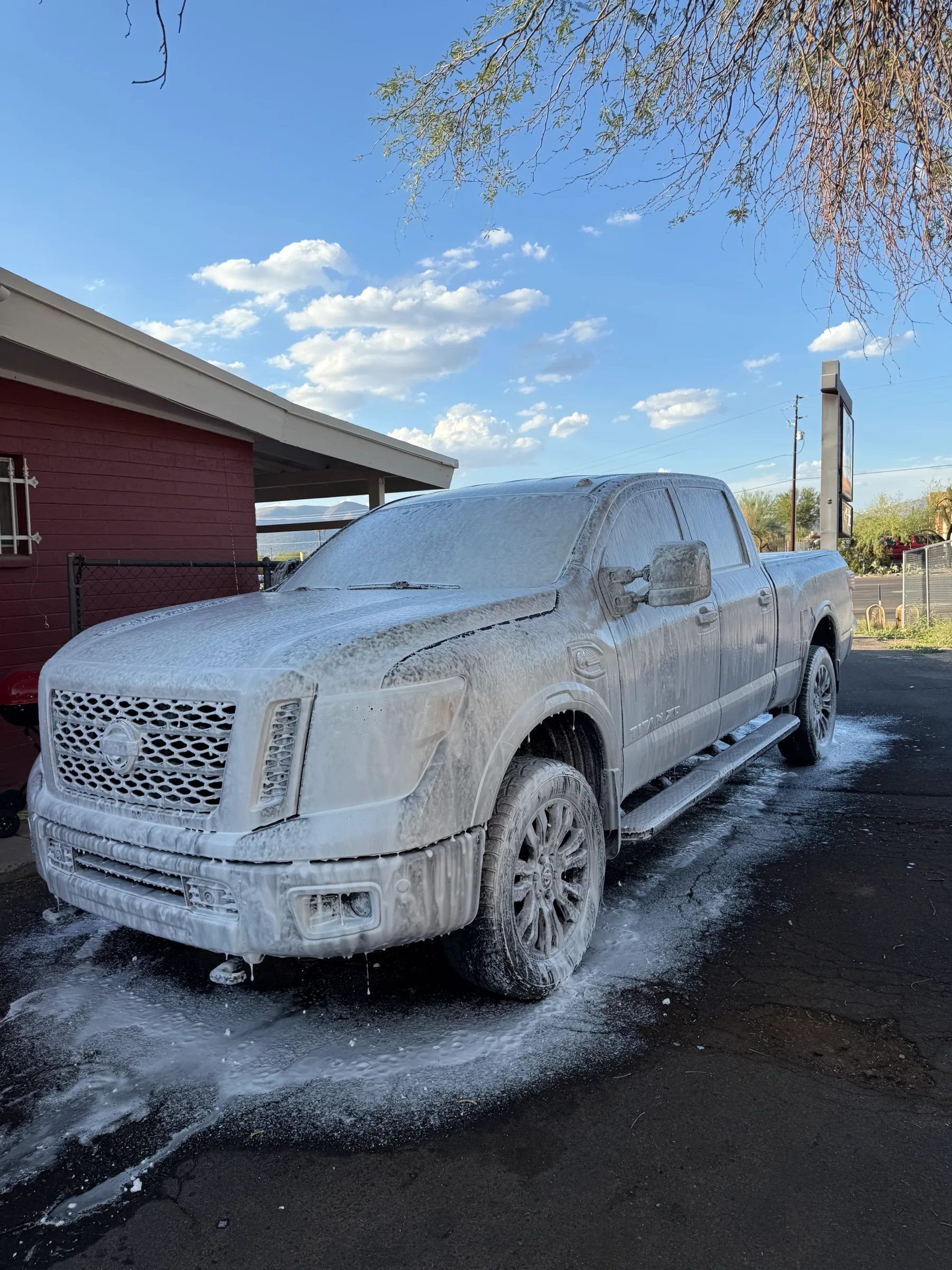A white Nissan Titan pickup truck covered in soapy water during a wash at a detailing facility in Cave Creek, Arizona.