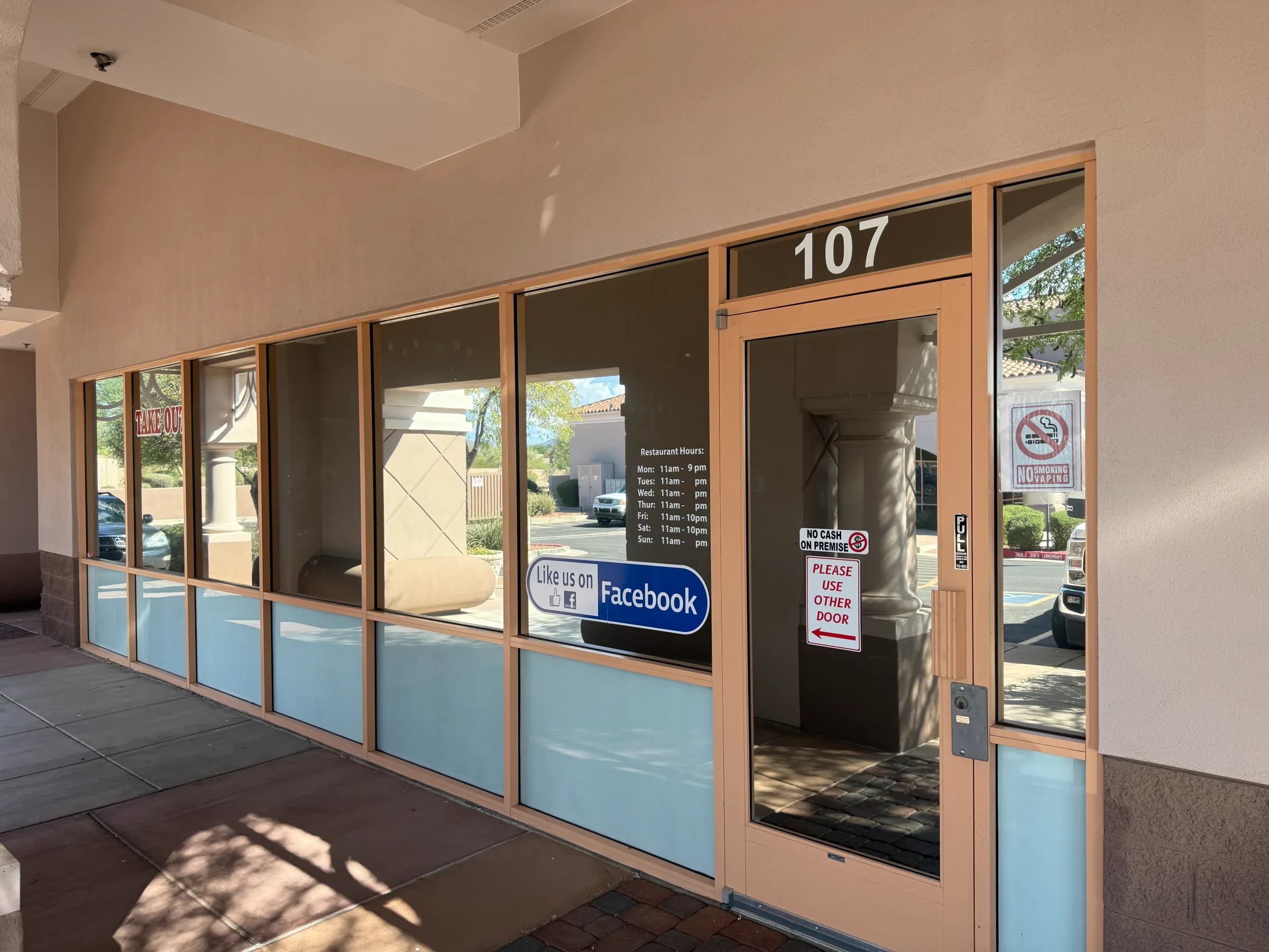 A commercial storefront with large windows featuring light blue window tint on the lower half of the glass panes and dark tint on the upper sections, with wood framing and a number 107 address marker.