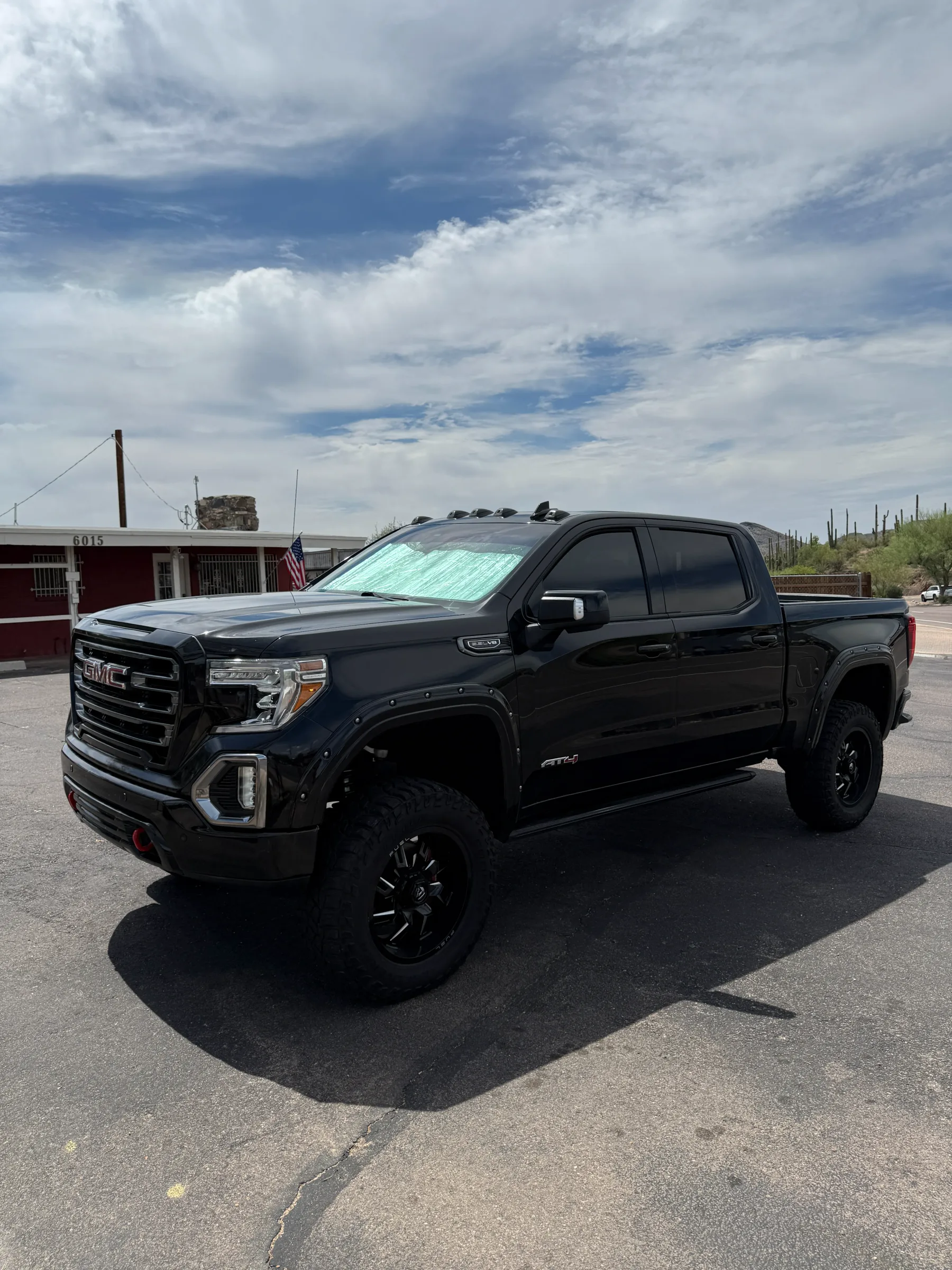 A black GMC Sierra pickup truck with dark window tint applied to all side windows, parked in a desert lot under a cloudy Arizona sky.