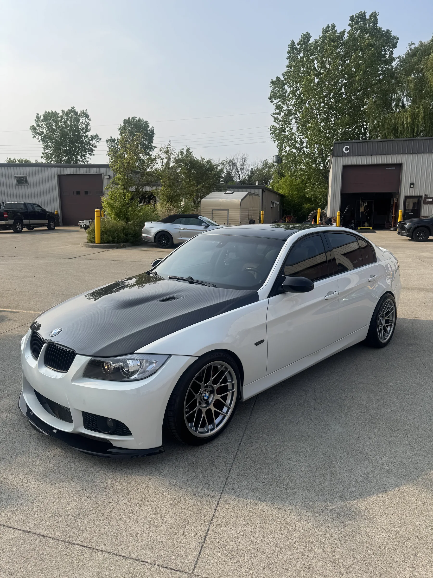 White BMW sedan with black racing stripe vinyl wrap parked at an automotive shop in Berea, Ohio.