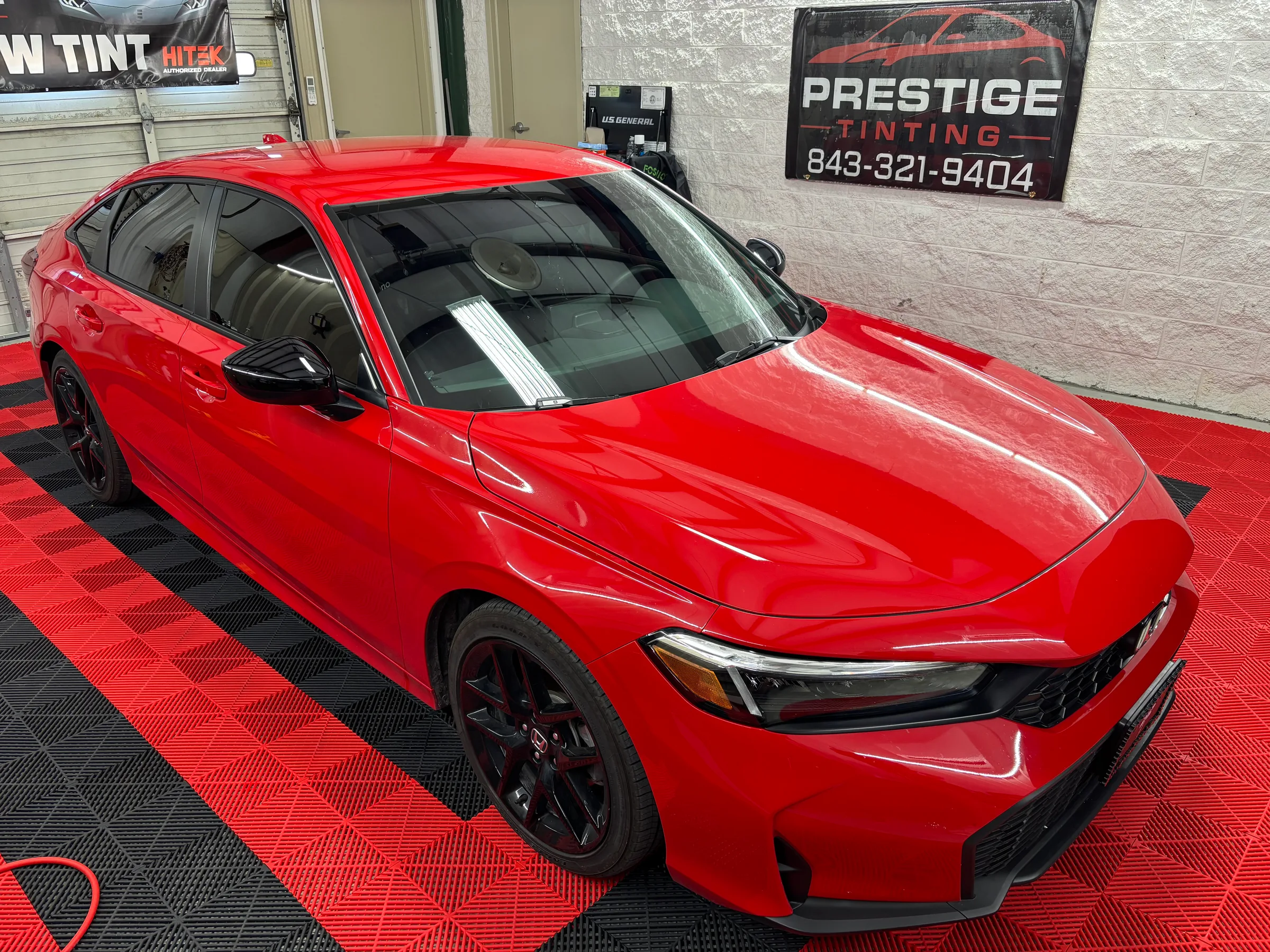 A bright red Honda Civic with dark window tint applied, displayed in a shop bay at Prestige Tinting in Conway, SC.