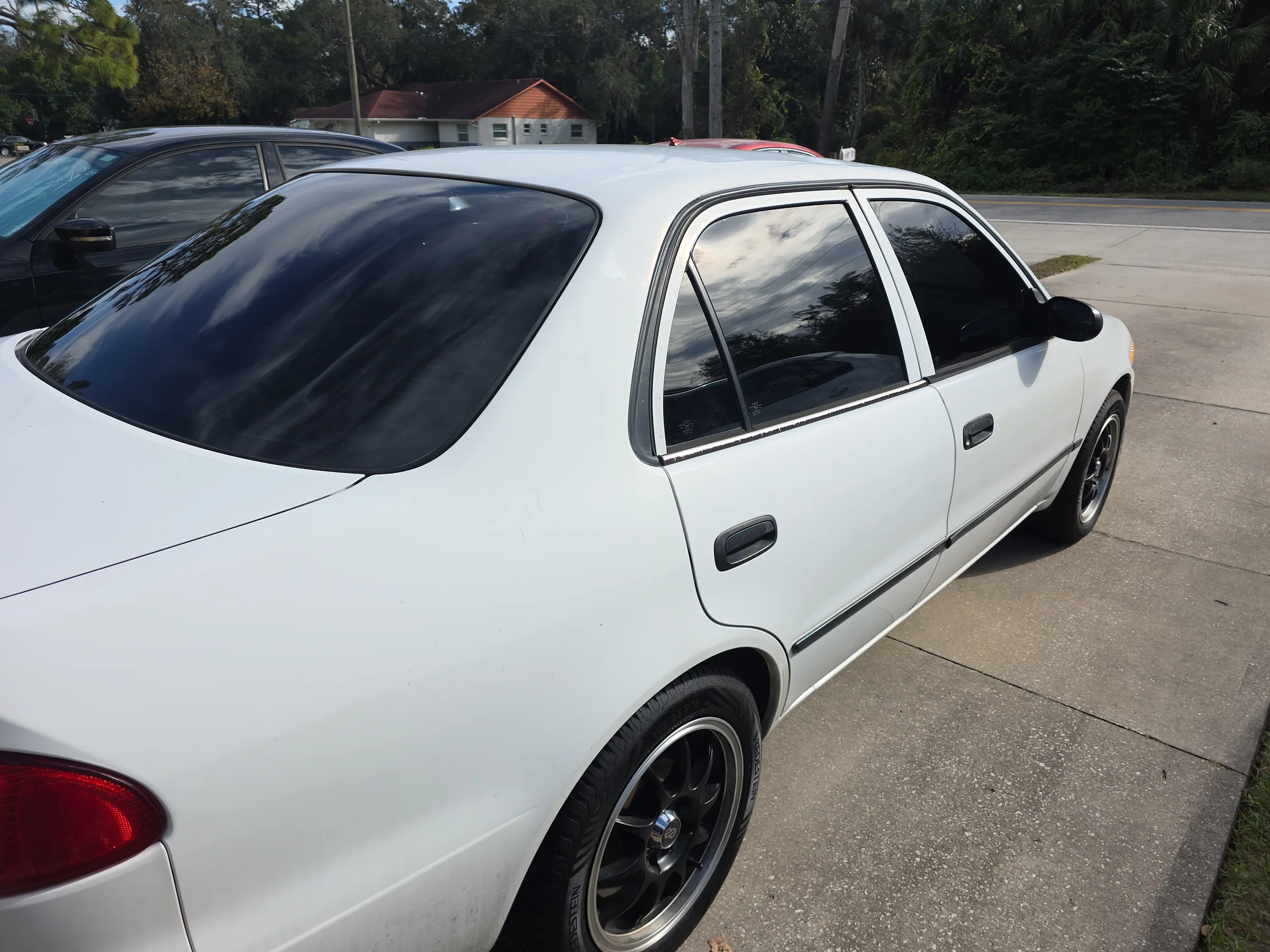 White four-door sedan with dark window tint applied to the rear and side windows, parked in a commercial lot.