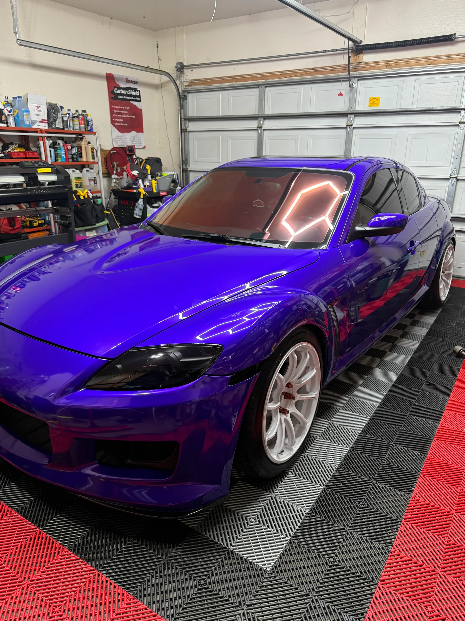 A vibrant purple Mazda RX-8 with dark window tint installed, displayed in a professional shop garage.