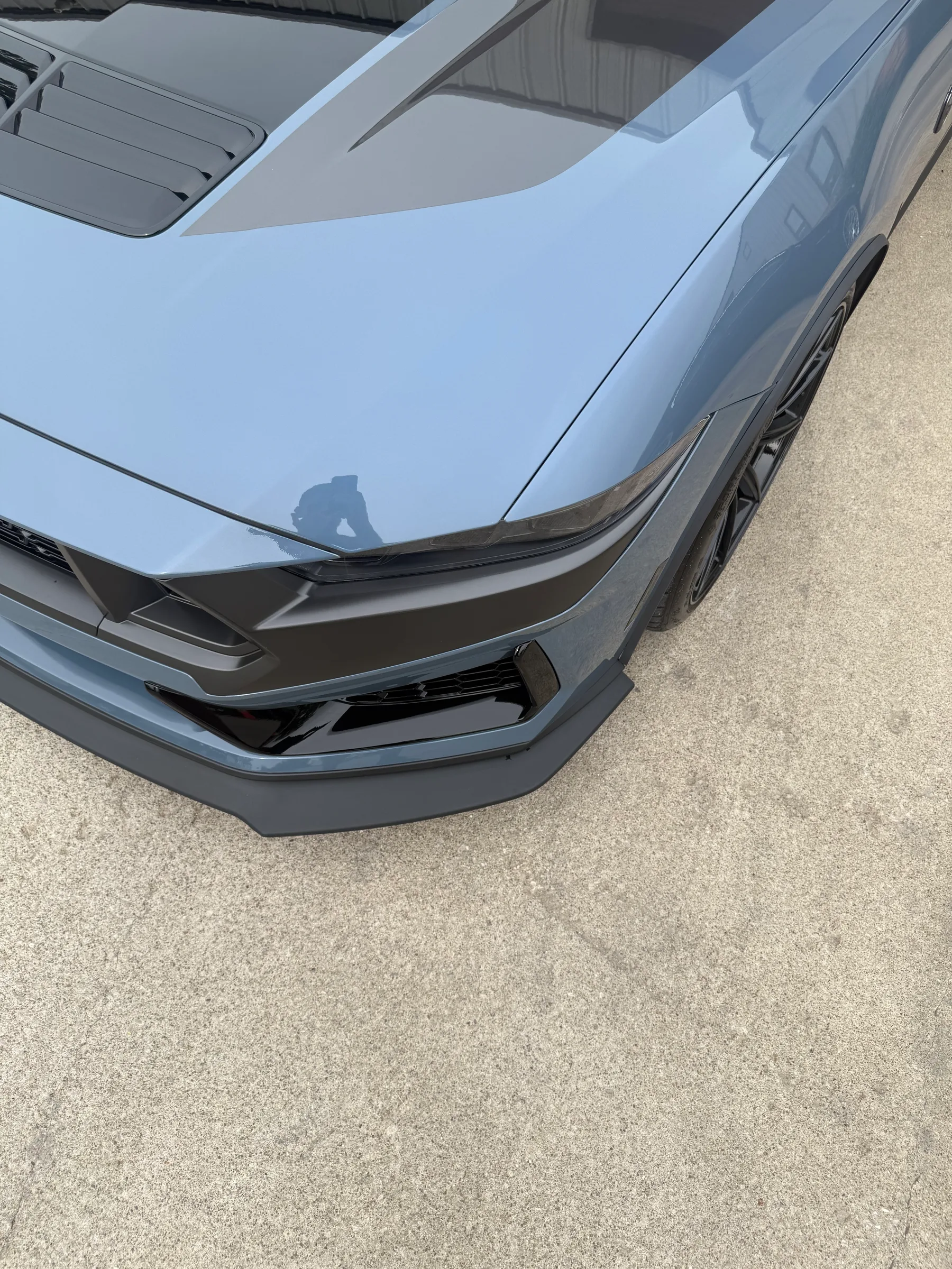 Close-up of a silver sedan's headlight area showing protective film applied to the headlight housing and front bumper.