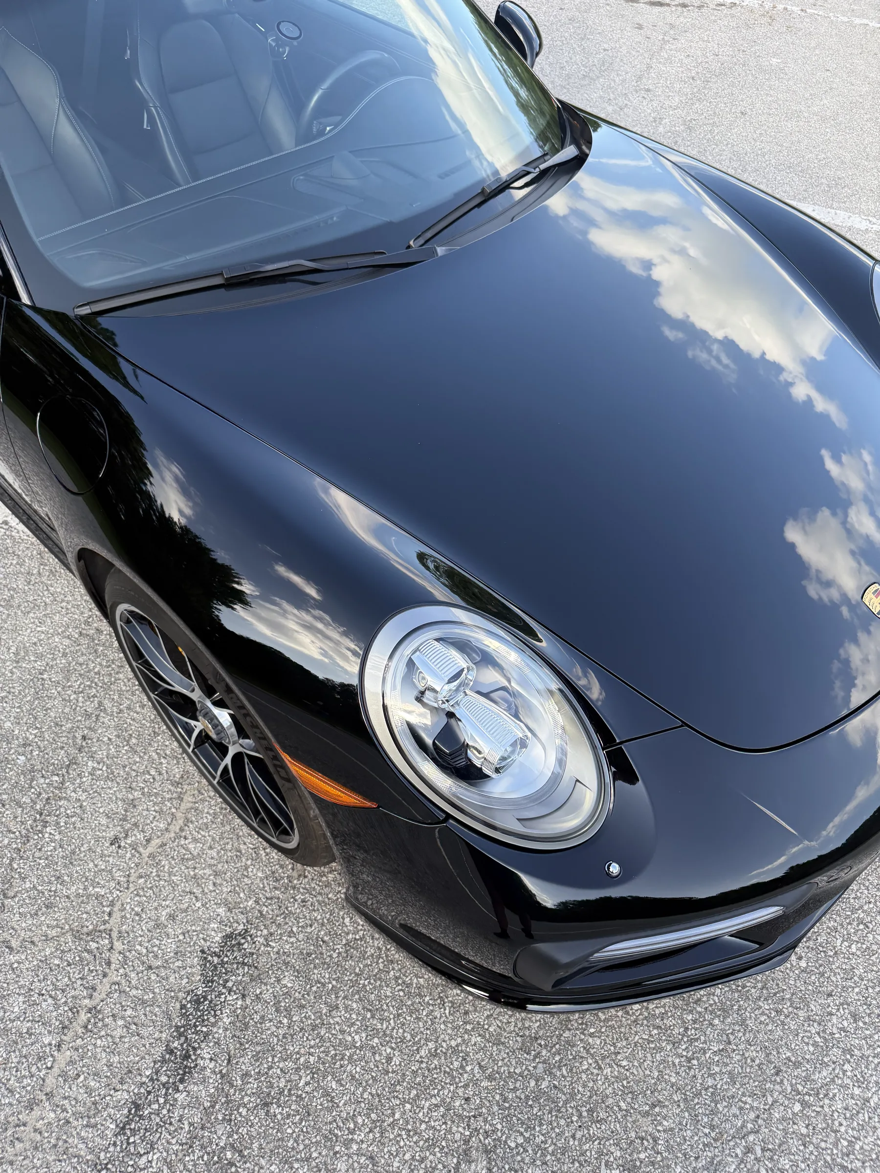 Overhead view of a black Porsche 911 with glossy ceramic-coated paintwork and chrome trim, parked on pavement.