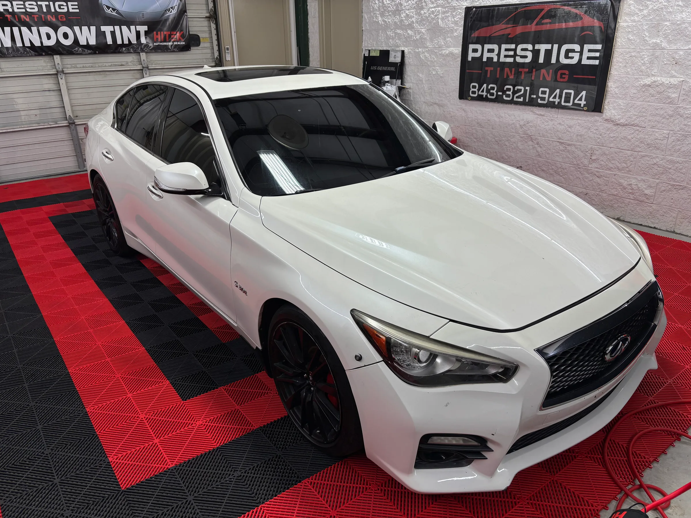 A white Infiniti Q50 with dark window tint installed, displayed in the showroom of Prestige Tinting in Conway, SC.