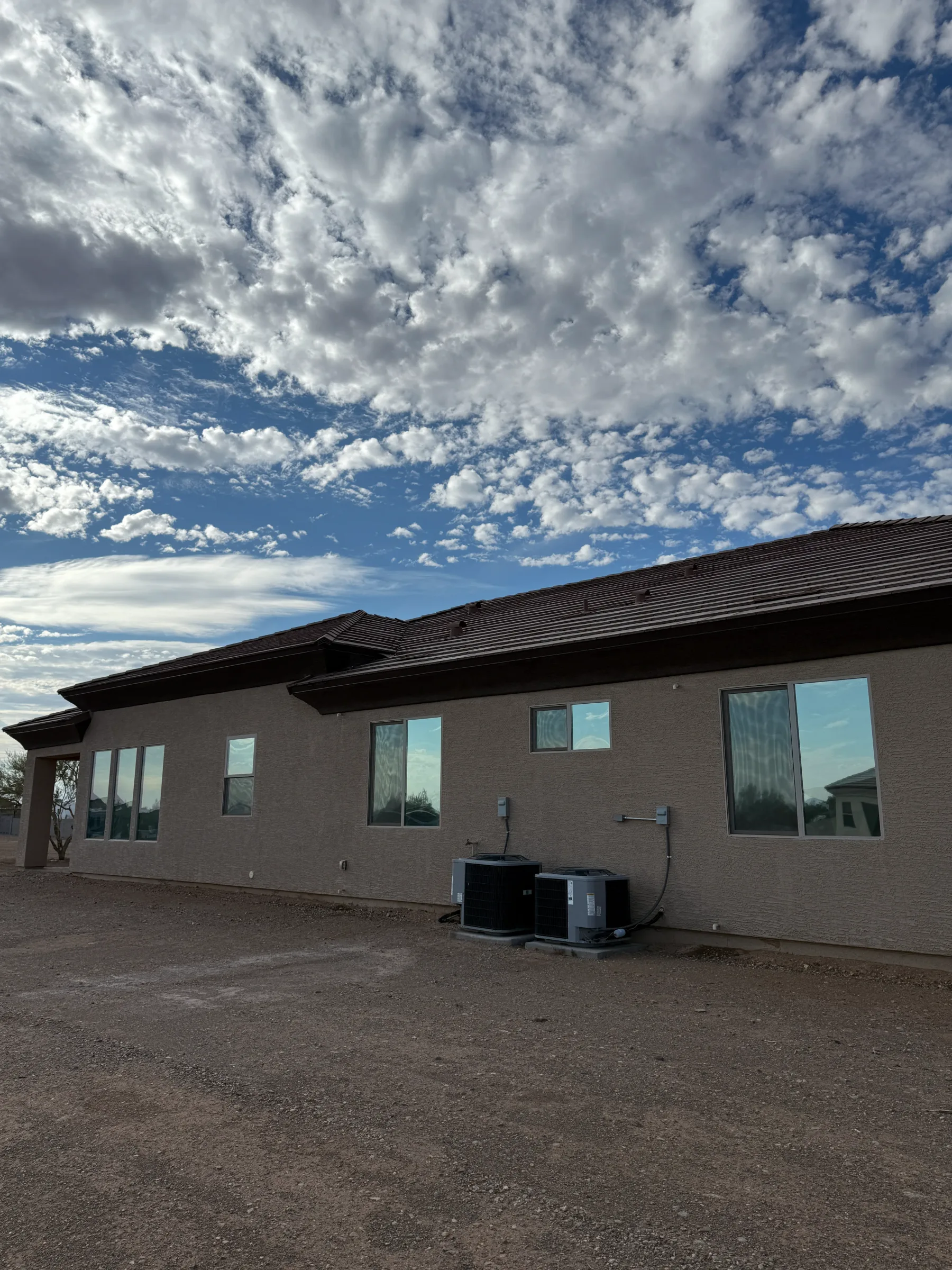 A modern brick residential home with large windows featuring window tint film applied to the glass, photographed against a dramatic Arizona sky with clouds.