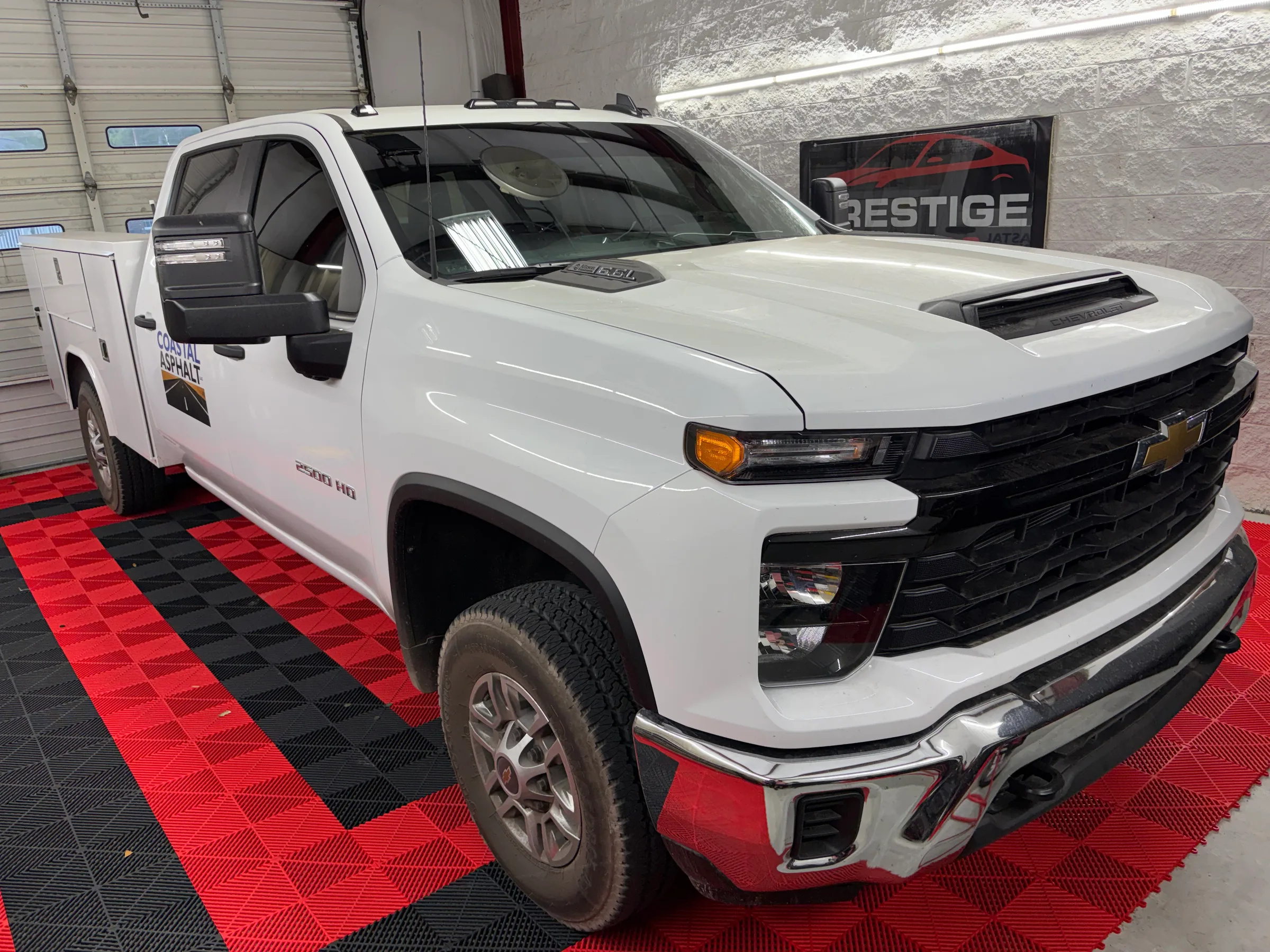 A white Chevrolet Silverado truck with dark window tint applied, displayed in a shop interior with red and black flooring.