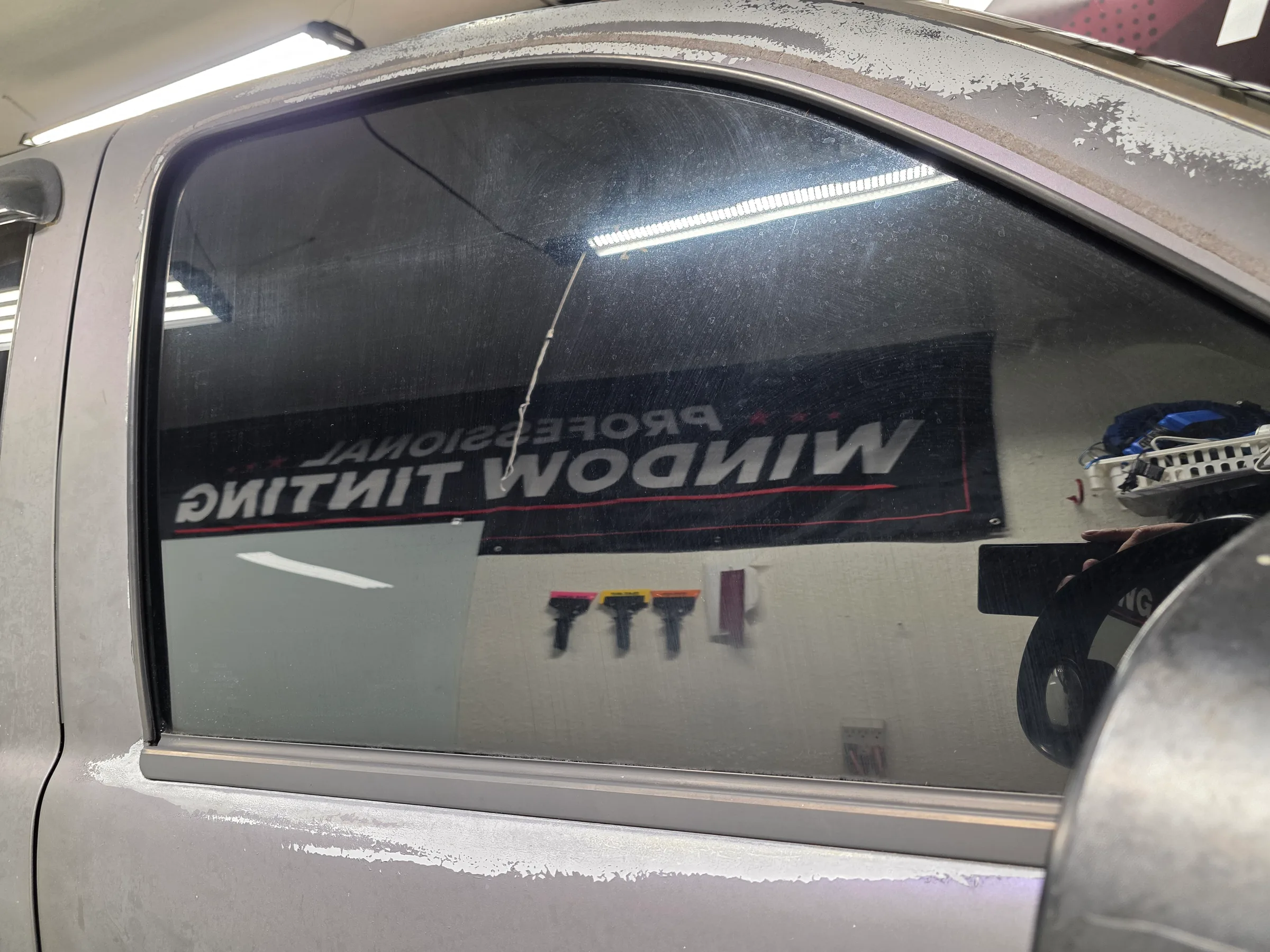 A truck window with dark window tint film being applied, showing the tinting process in progress at an automotive shop.