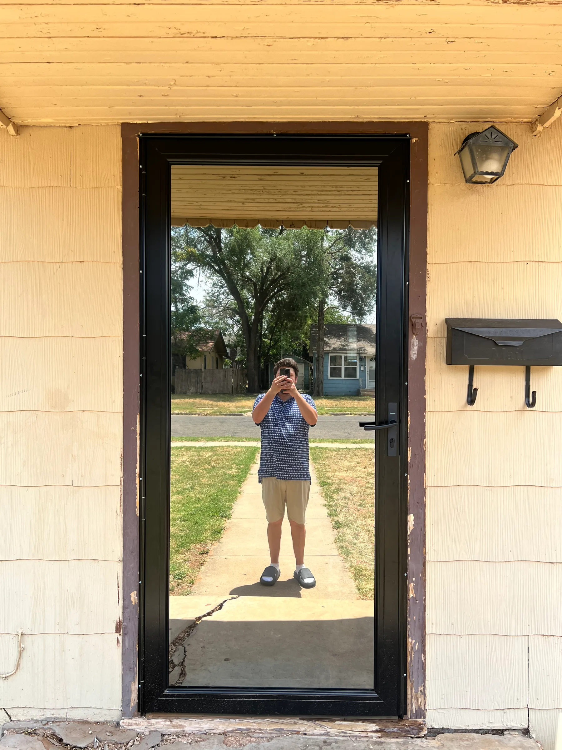 A residential front door with a black frame and clear glass pane allowing a view through to the exterior.