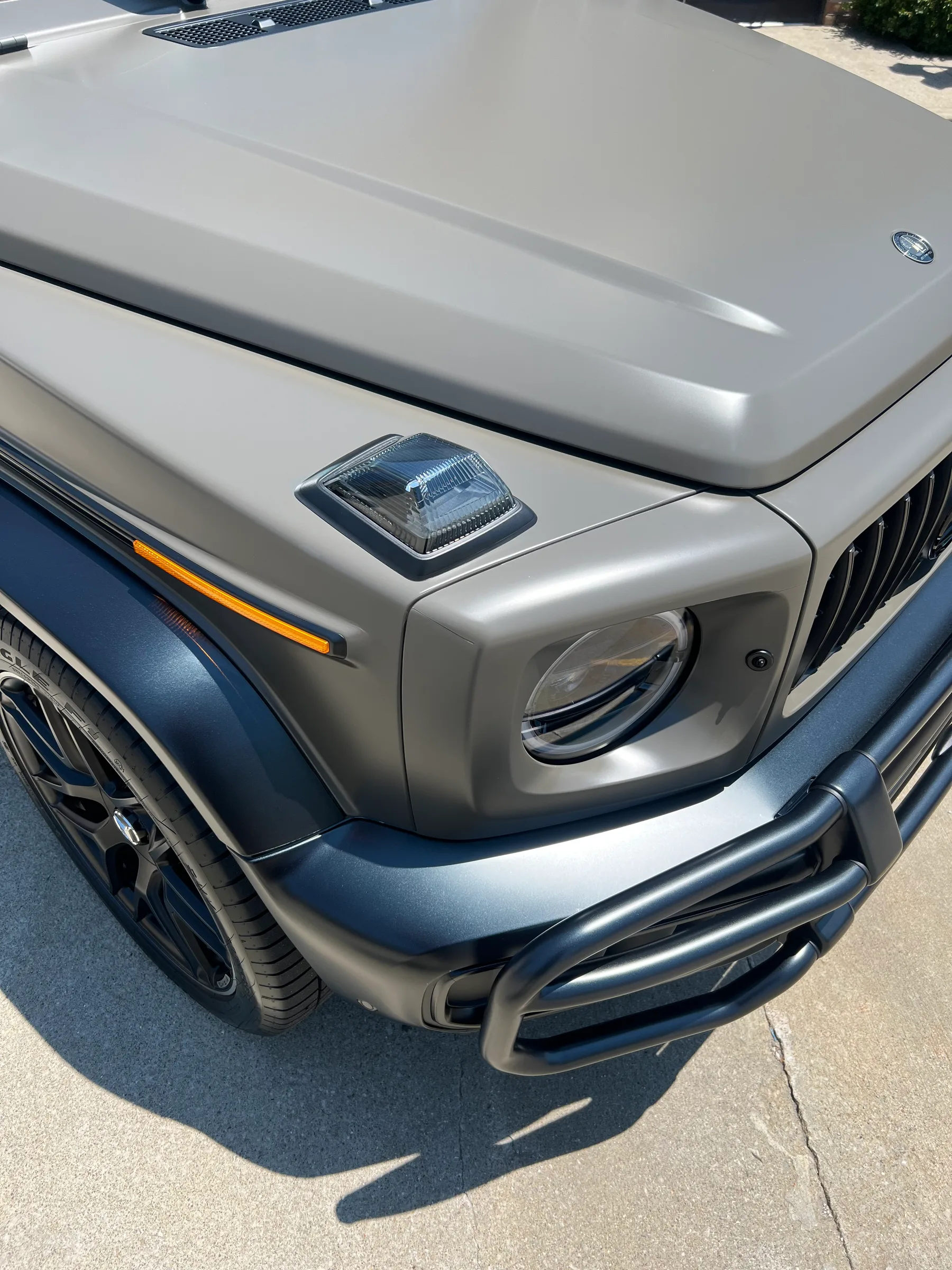 A silver and blue Jeep with clear protective film applied to the headlights and hood.