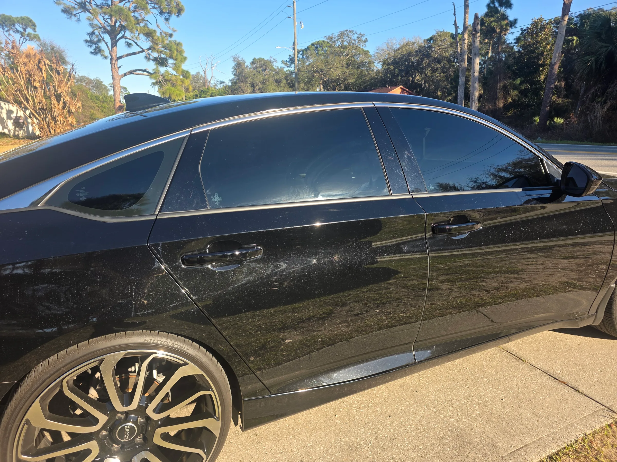 A black sedan with dark window tint applied to all windows, parked on a residential driveway.