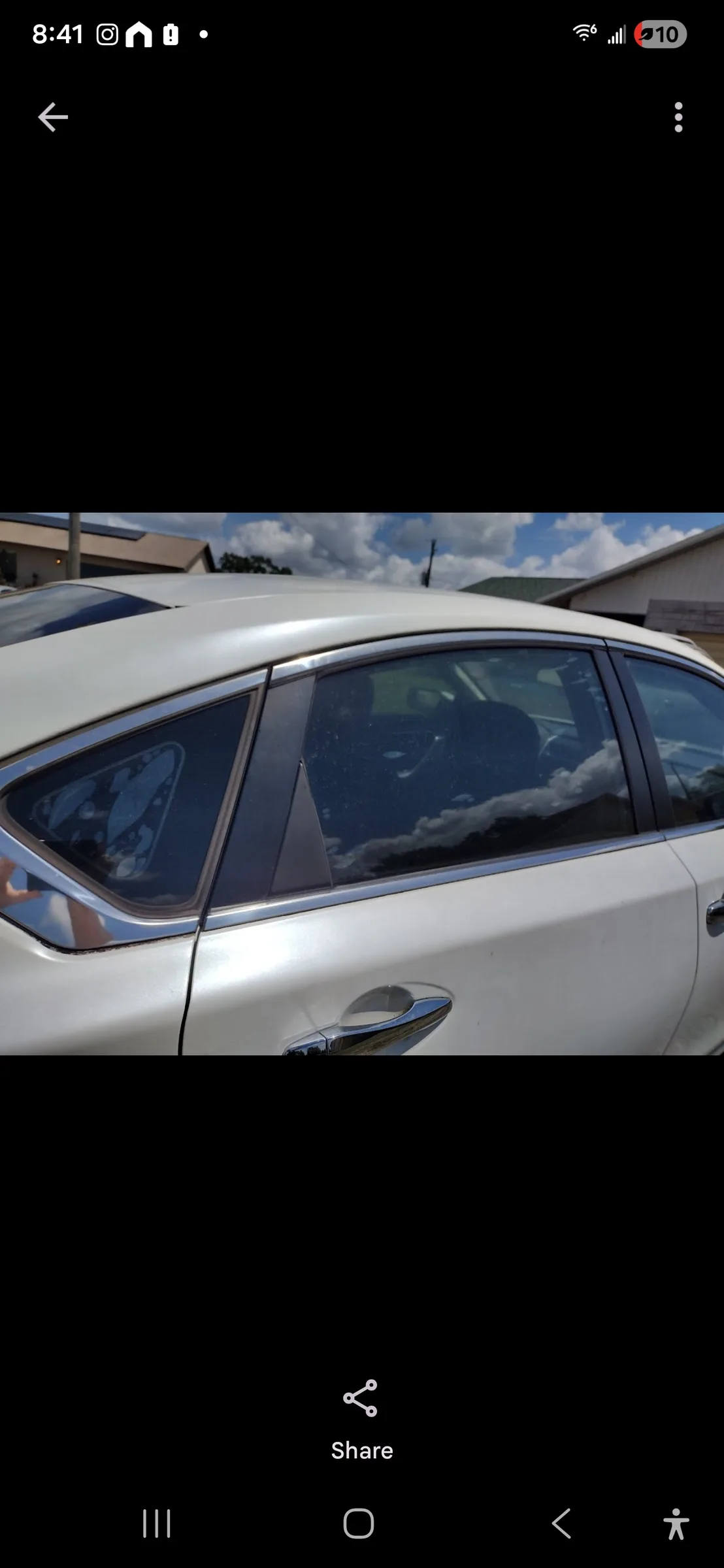 A white sedan with dark window tint applied to the rear and side windows, parked outdoors with buildings visible in the background.