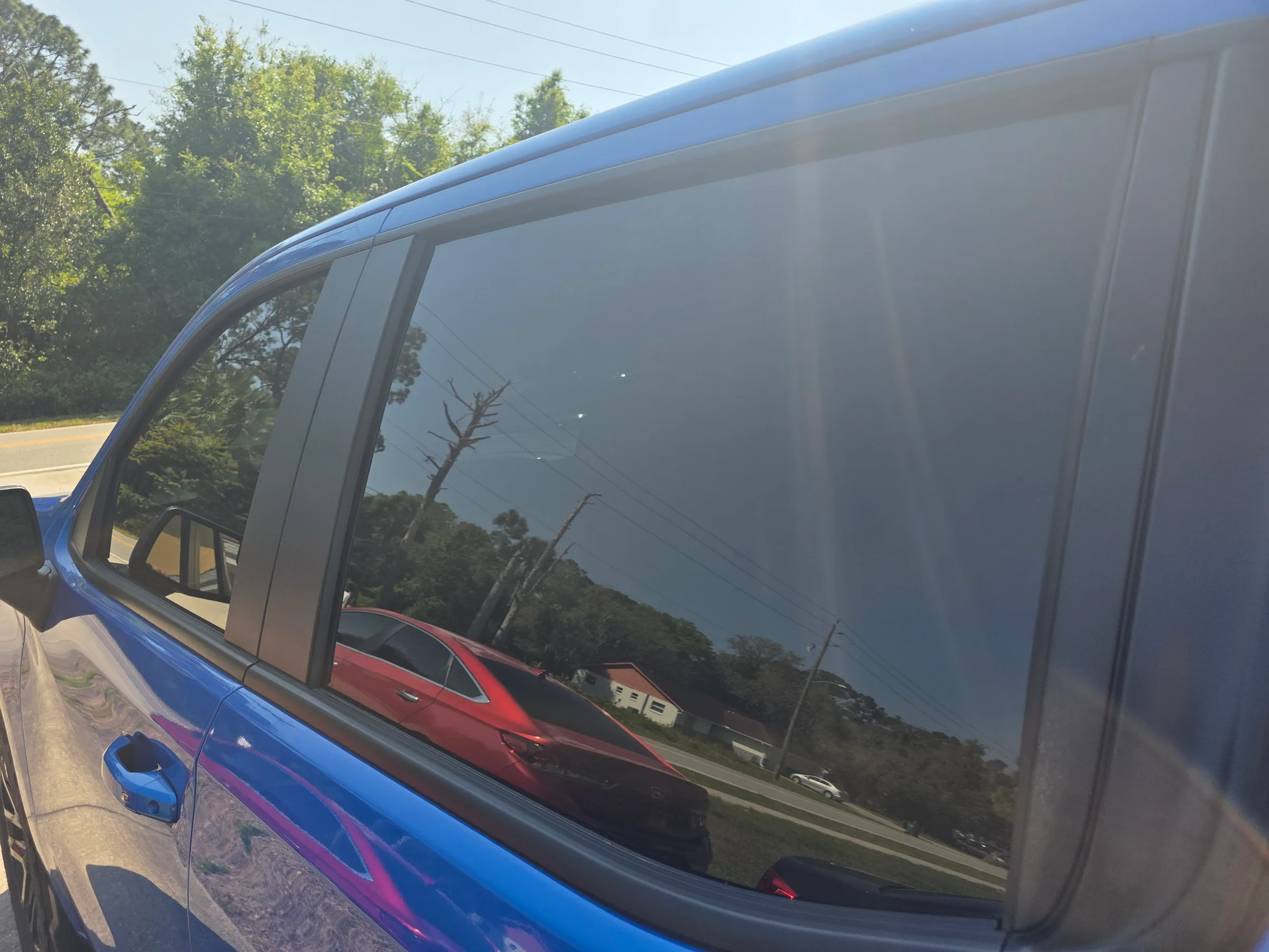 A blue van with dark window tint applied to the rear side windows, showing the tint's light-blocking effect in bright daylight.