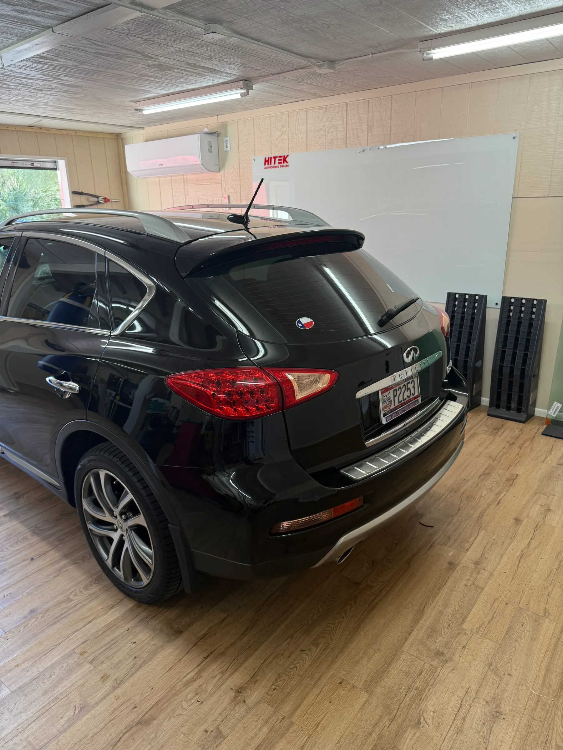 Black Infiniti SUV with tinted windows parked inside a professional automotive service bay.