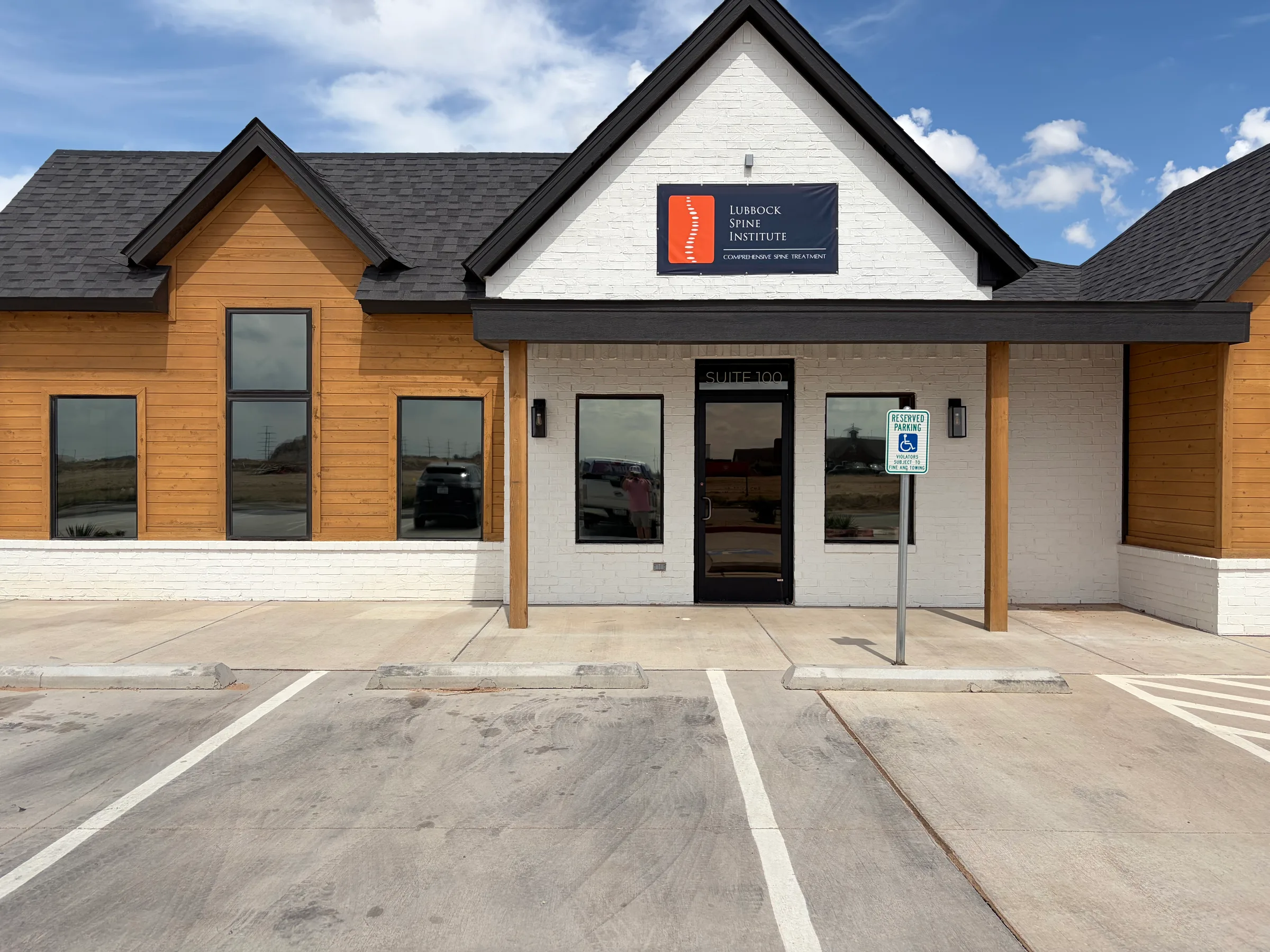 Front exterior of the Lubbock Spine Institute medical office building with modern architecture, white brick and wood siding, large windows, and a professional signage in Lubbock, Texas.