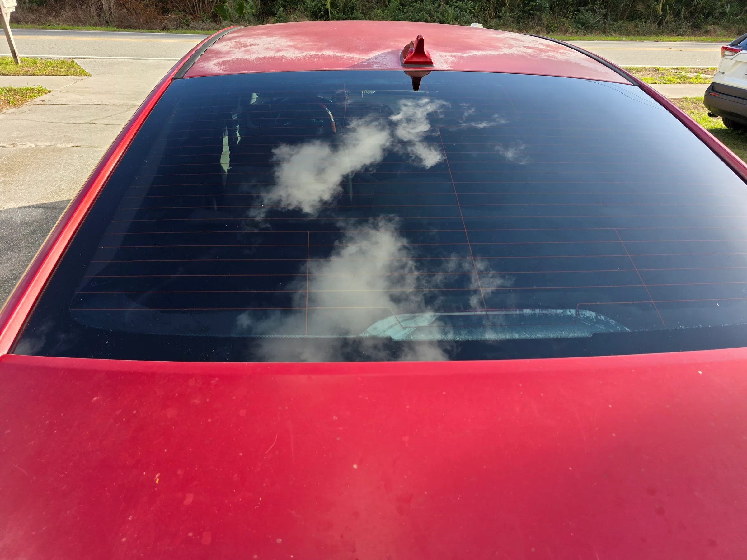 A red truck with dark tinted rear window, parked in a lot with sky and clouds reflected in the glass.