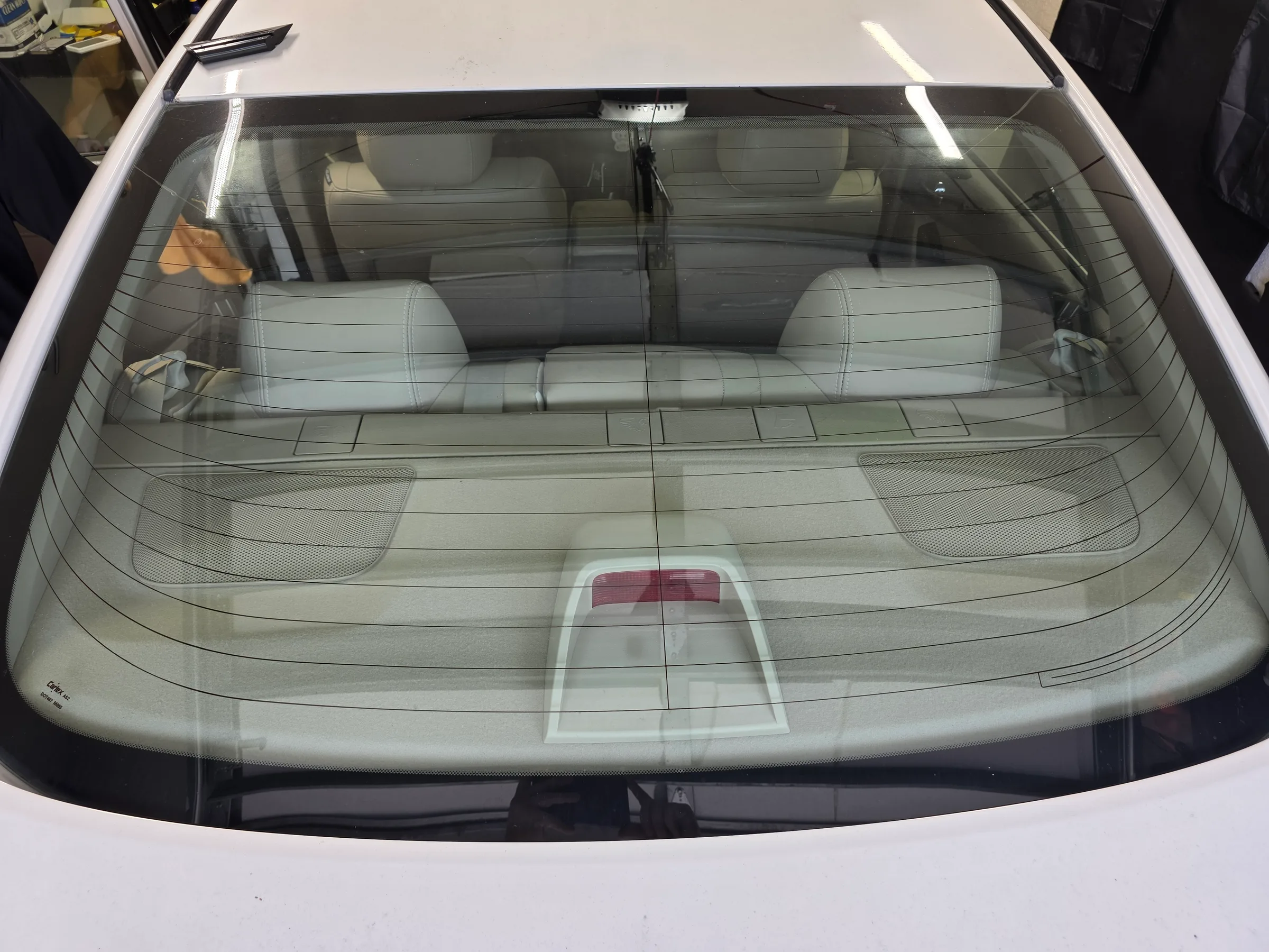 A rear windshield with light-tinted window film applied, showing the interior of a white vehicle with visible seating and interior protection.