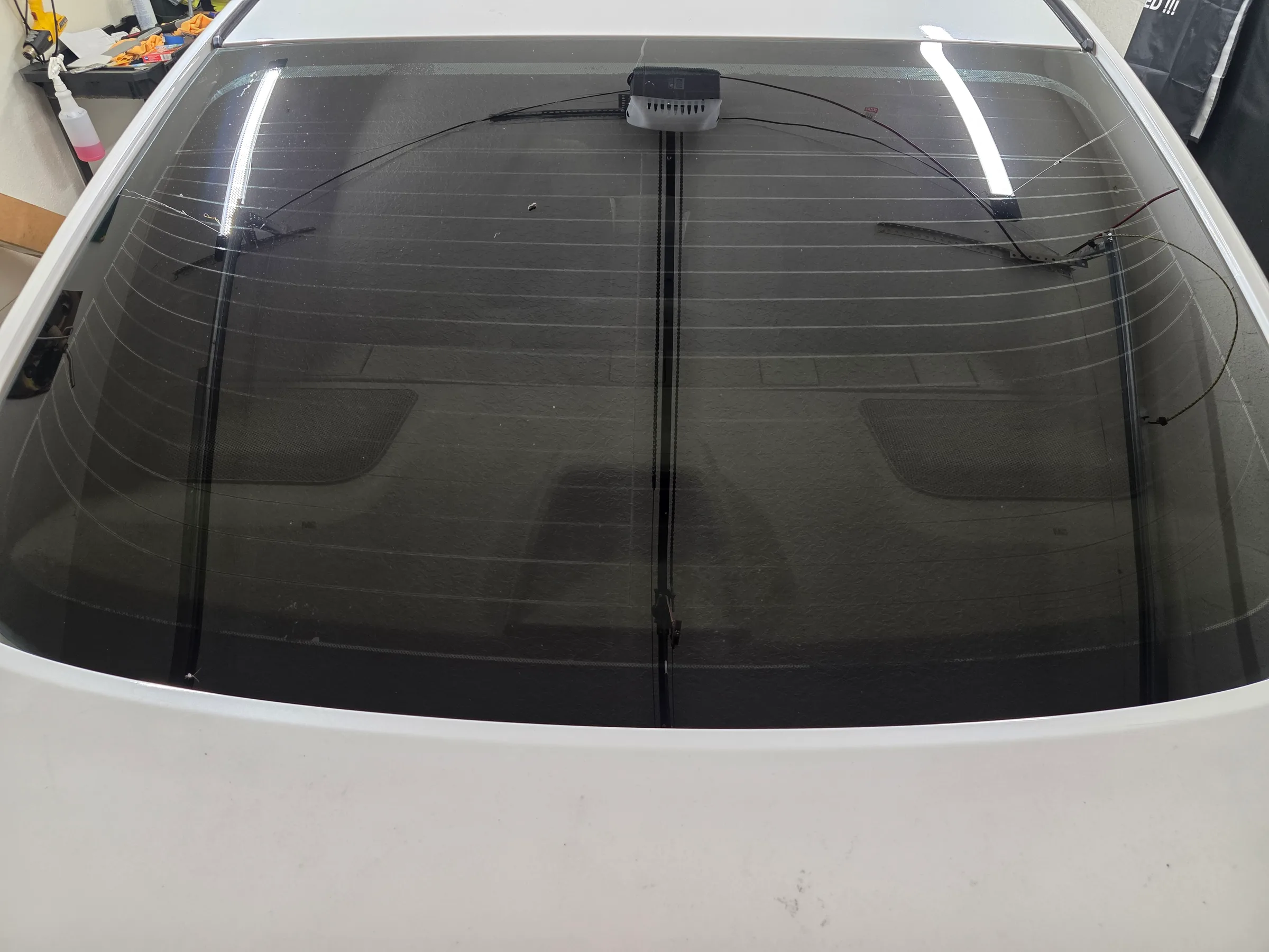 A white vehicle's rear windshield with dark window tint applied, shown from above in an installation bay.