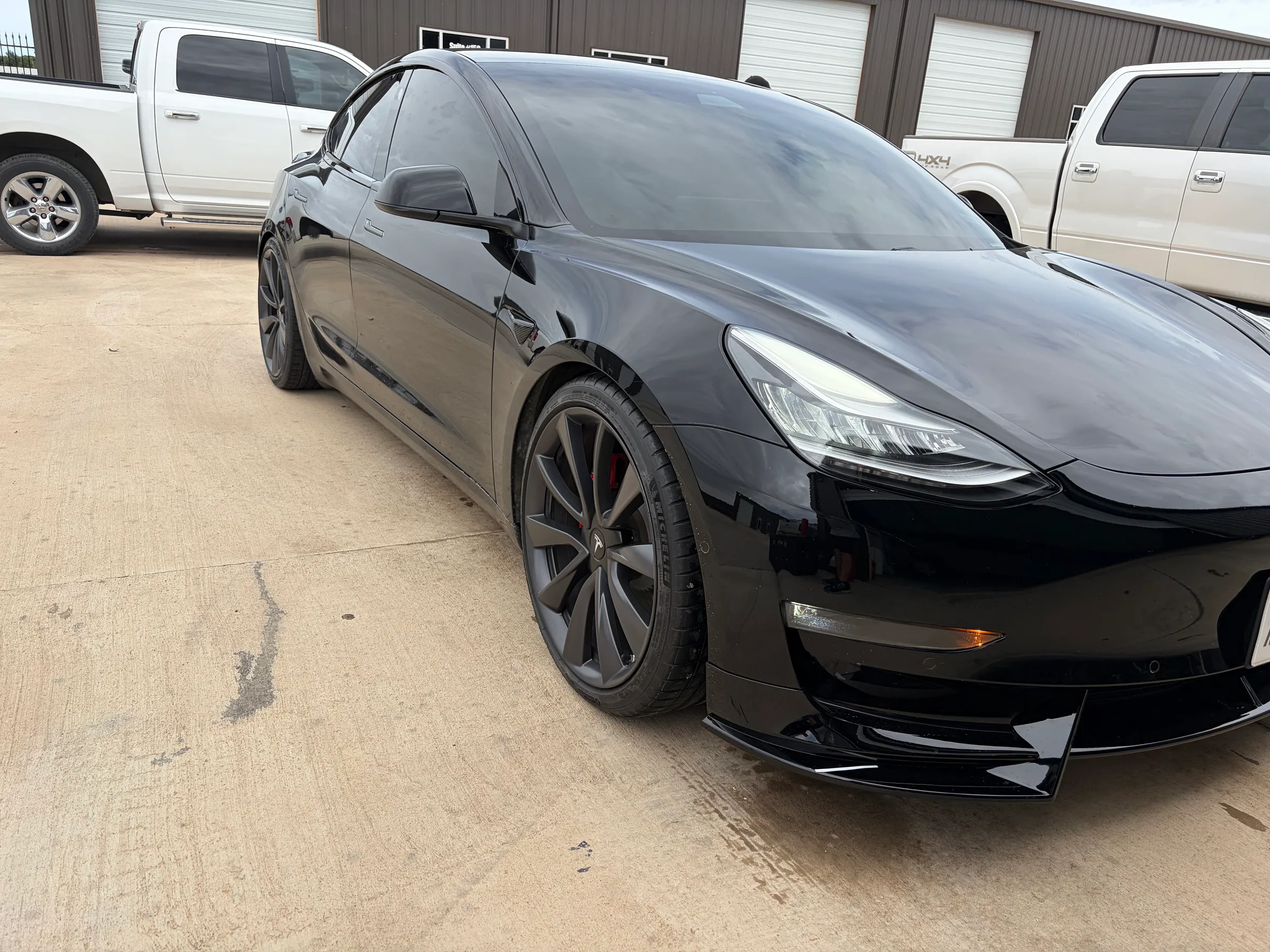 A black Tesla Model 3 with tinted windows parked in front of an automotive service facility in Lubbock.