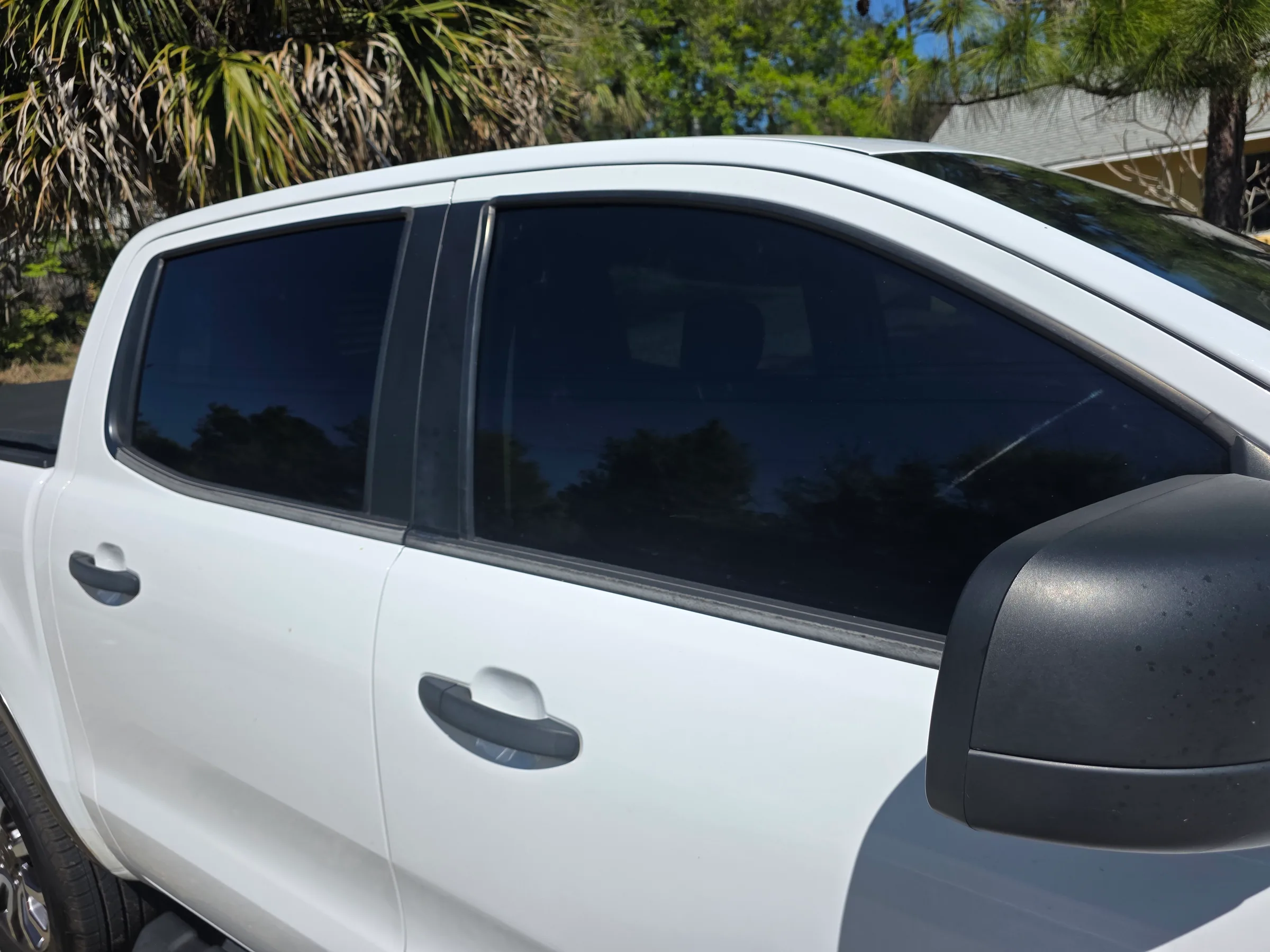 A white pickup truck with dark window tint applied to the cab windows and rear glass, photographed outdoors with palm trees in the background.