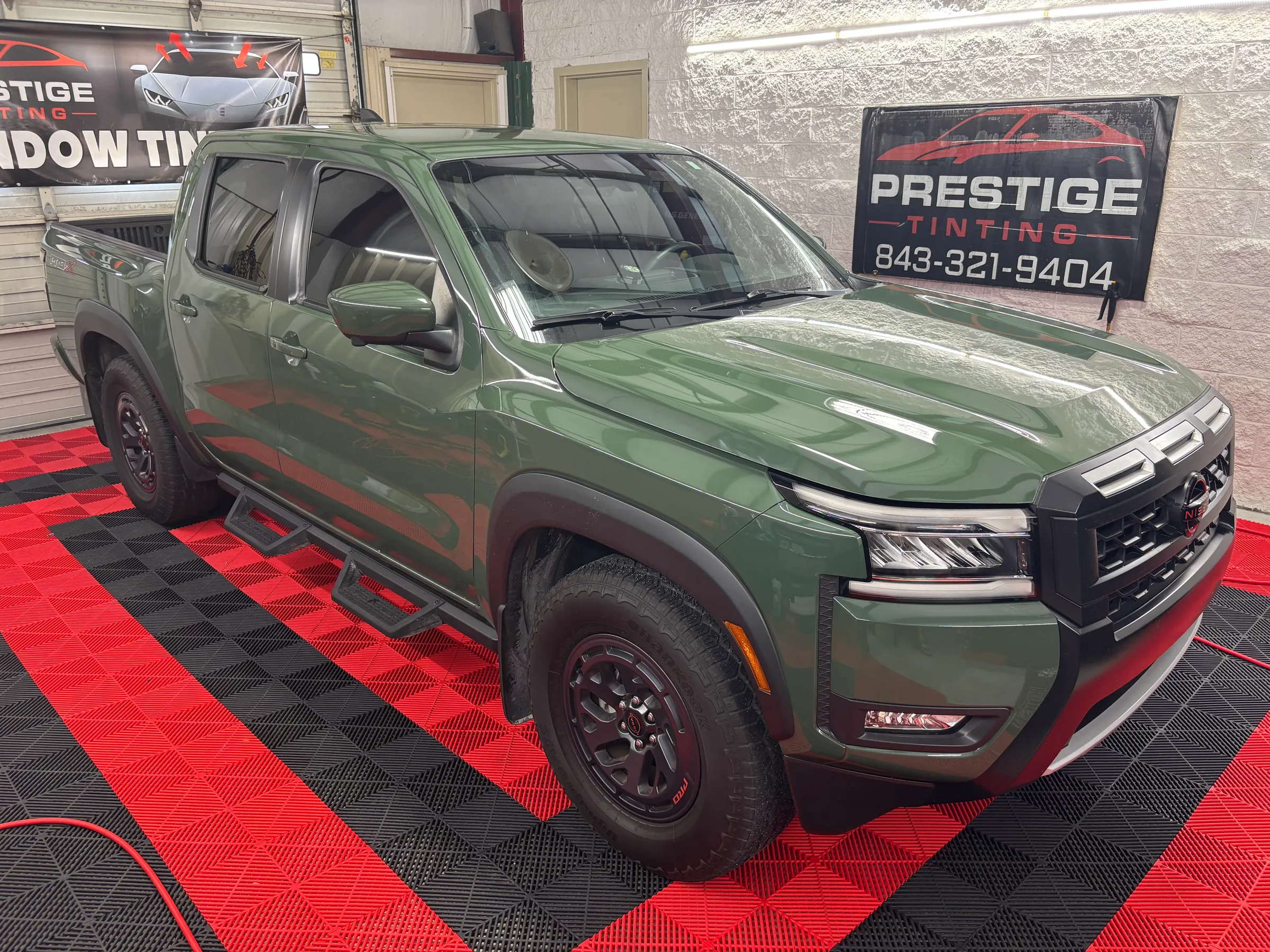 A green GMC Sierra pickup truck with tinted windows displayed in the Prestige Tinting showroom in Conway.