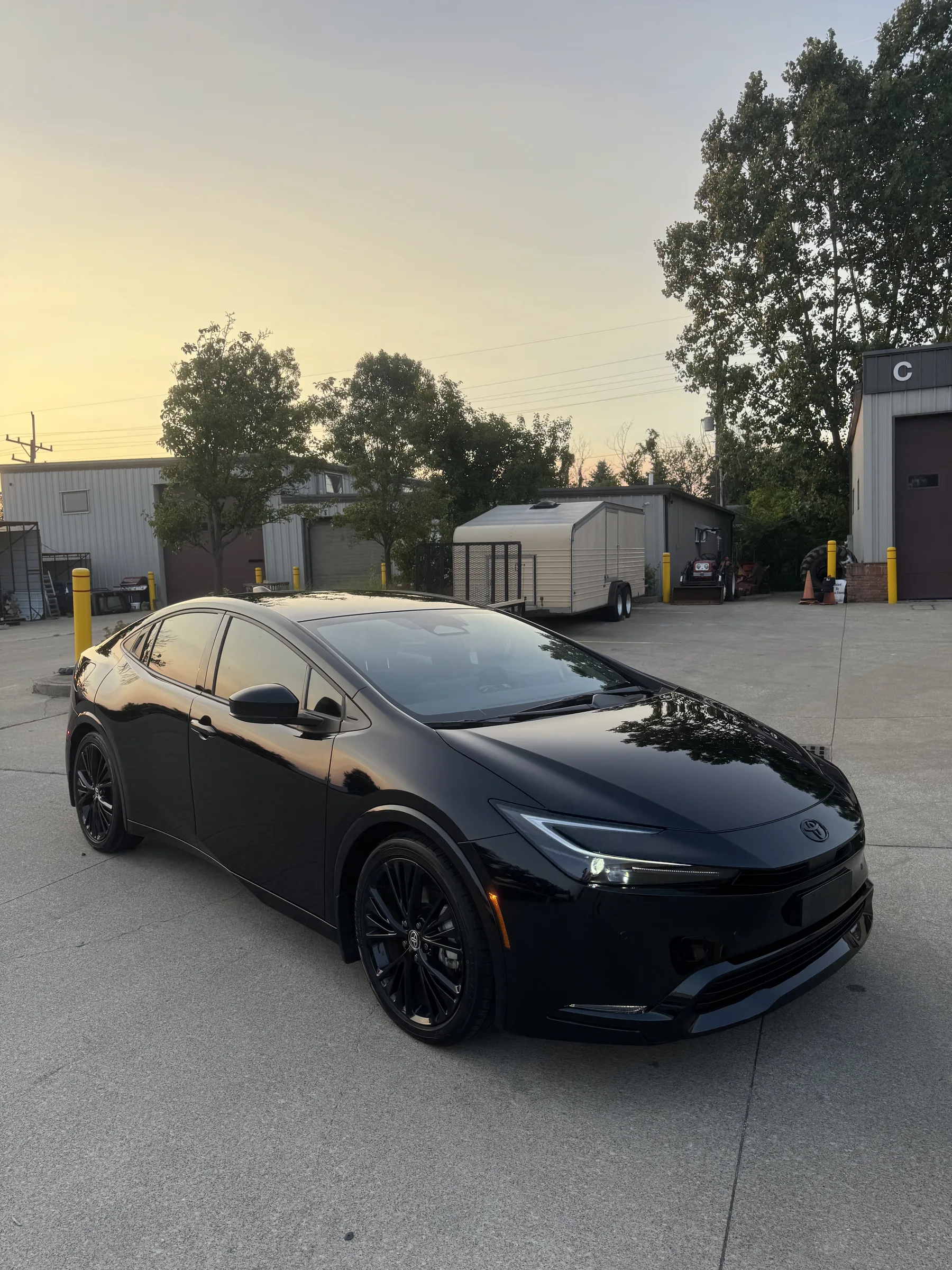 A black Toyota Prius parked on a concrete lot at an auto shop facility in Berea, Ohio, with industrial buildings and yellow bollards visible in the background.
