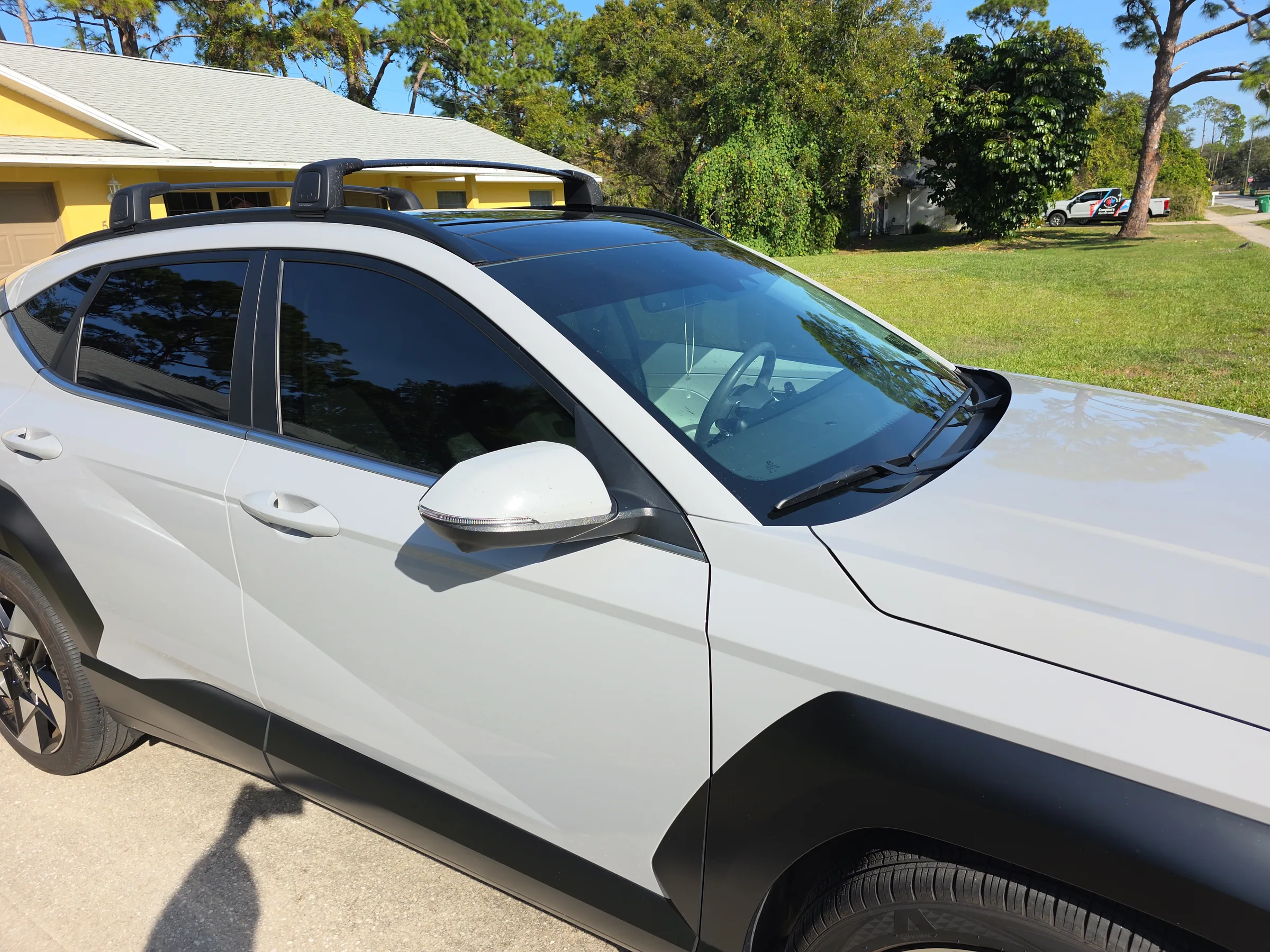 A white SUV with dark window tint applied to all side and rear windows, parked in front of a yellow building.