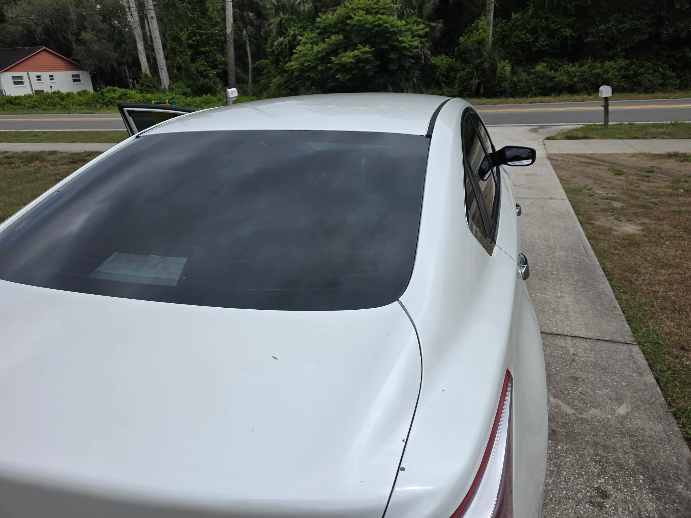 White sedan with dark window tint applied to the rear and side windows, parked outdoors near a residential area.