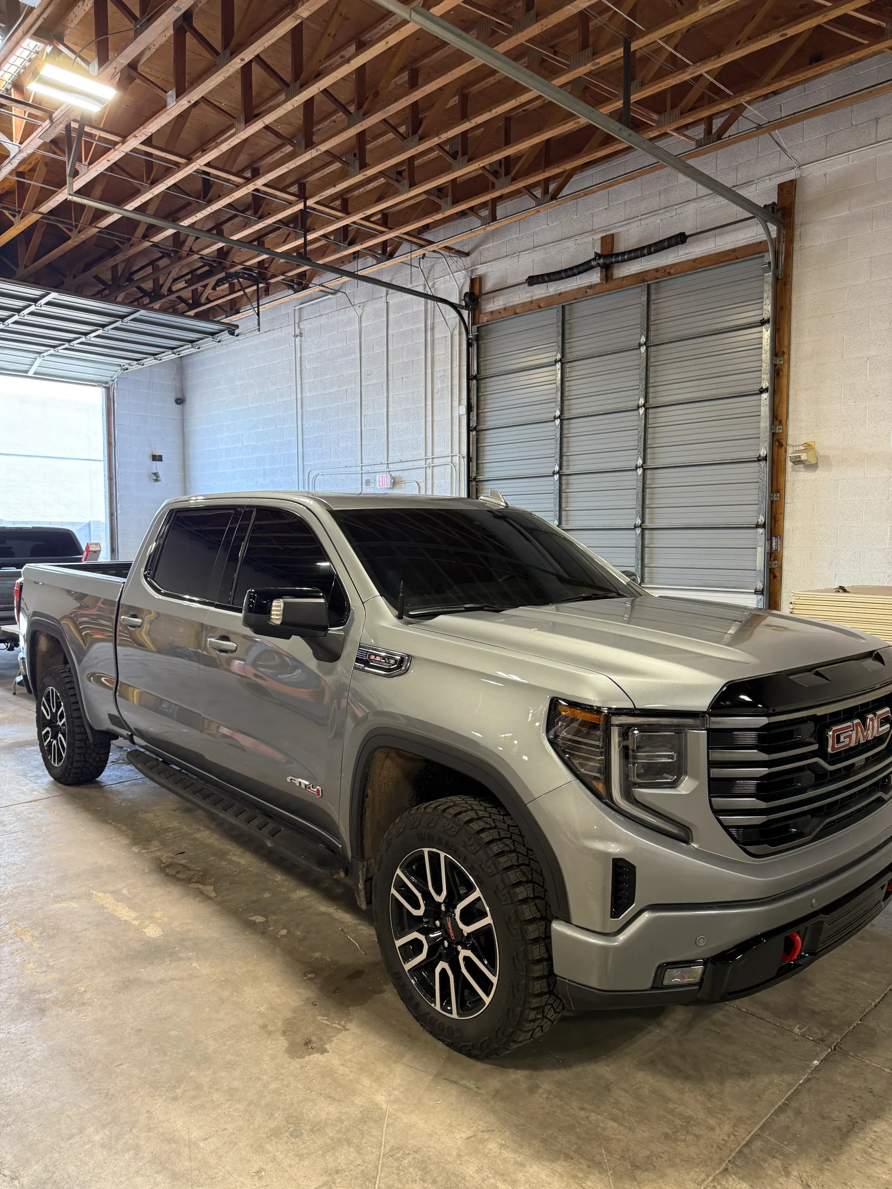 Silver GMC Sierra pickup truck with dark window tint applied, parked in a service bay at an automotive shop in Cave Creek.