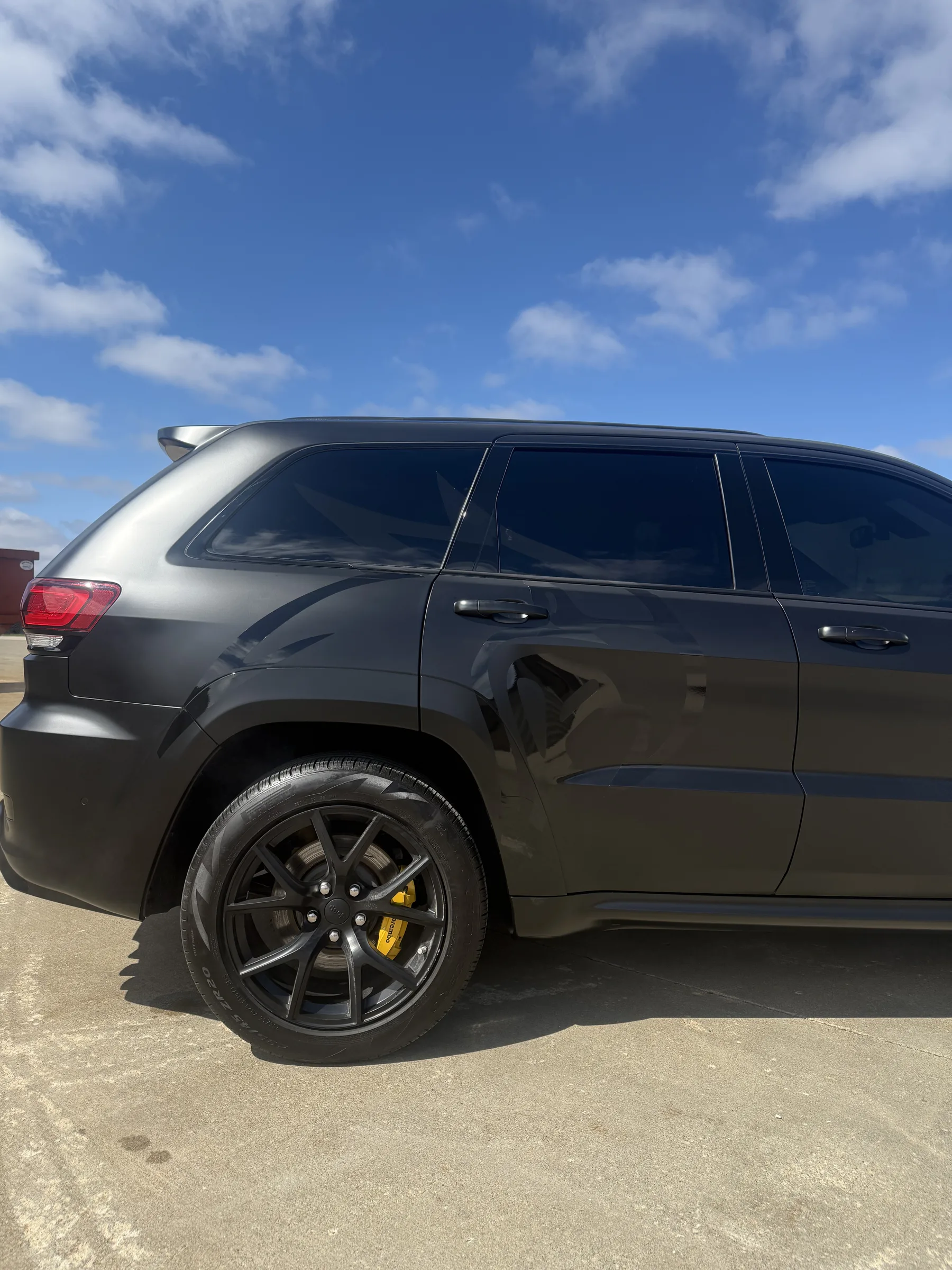 Black SUV with dark window tint and custom wheels parked outdoors under a clear blue sky.