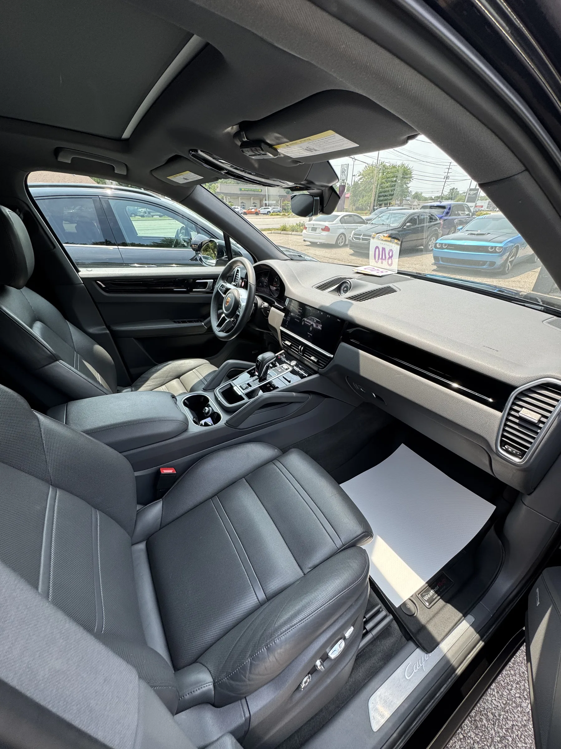 Interior view of a Porsche showing leather seats and dashboard with protective film applied to the floor mats and door sill area.