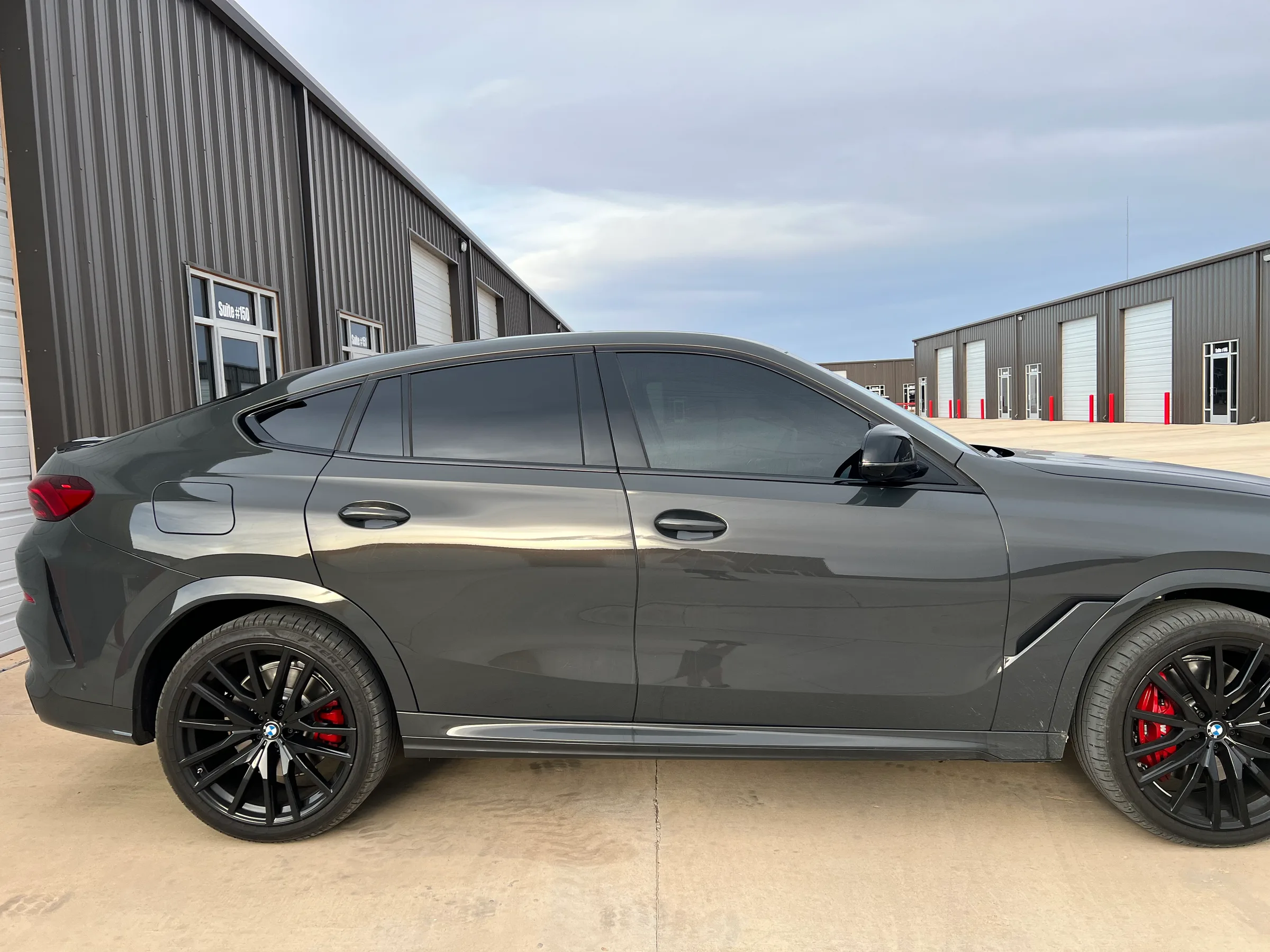 Gray BMW X6 SUV with tinted windows parked at a commercial facility, showing the passenger side profile with dark-tinted glass and custom wheels.