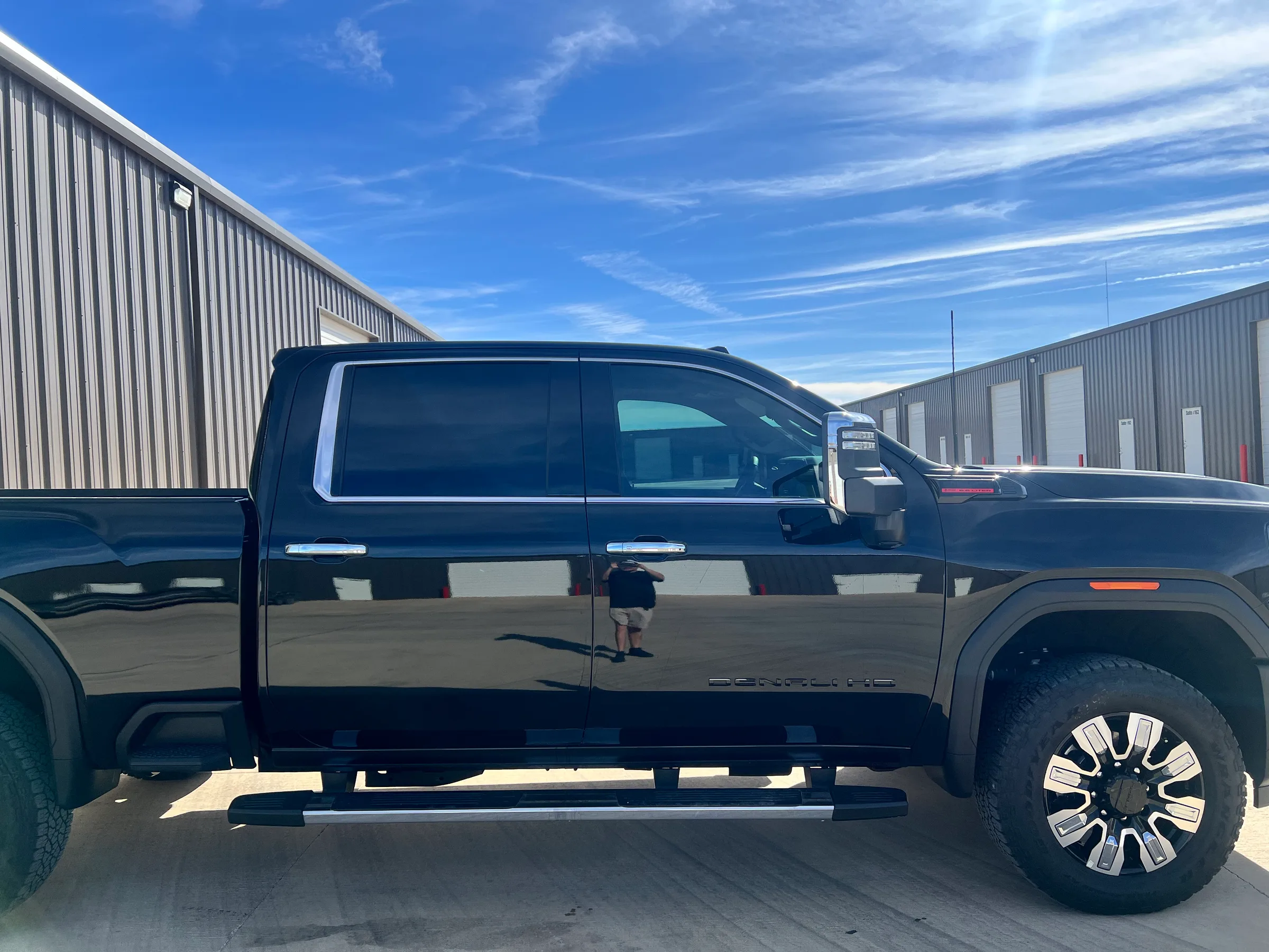 Passenger side view of a black GMC 2500 pickup truck with dark window tinting applied, parked outside a metal warehouse building.