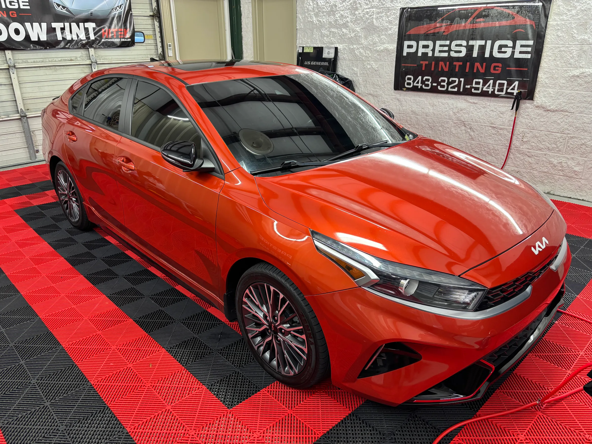 A red Kia sedan with dark window tint applied, displayed in a shop bay at Prestige Tinting in Conway, SC.