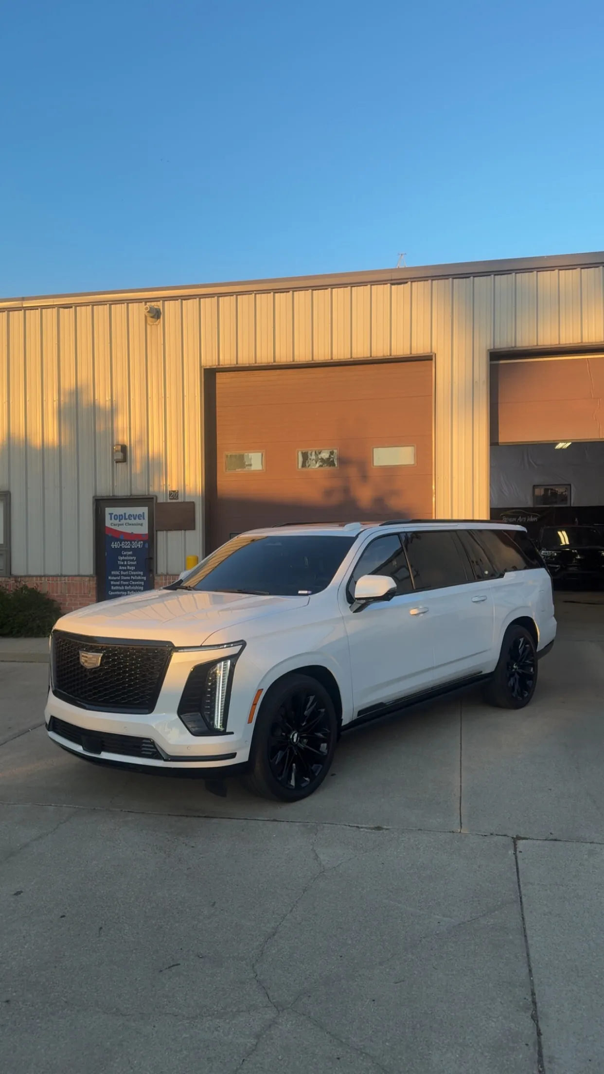 A white Cadillac Escalade SUV with dark window tinting parked in front of an industrial building in Berea, Ohio.