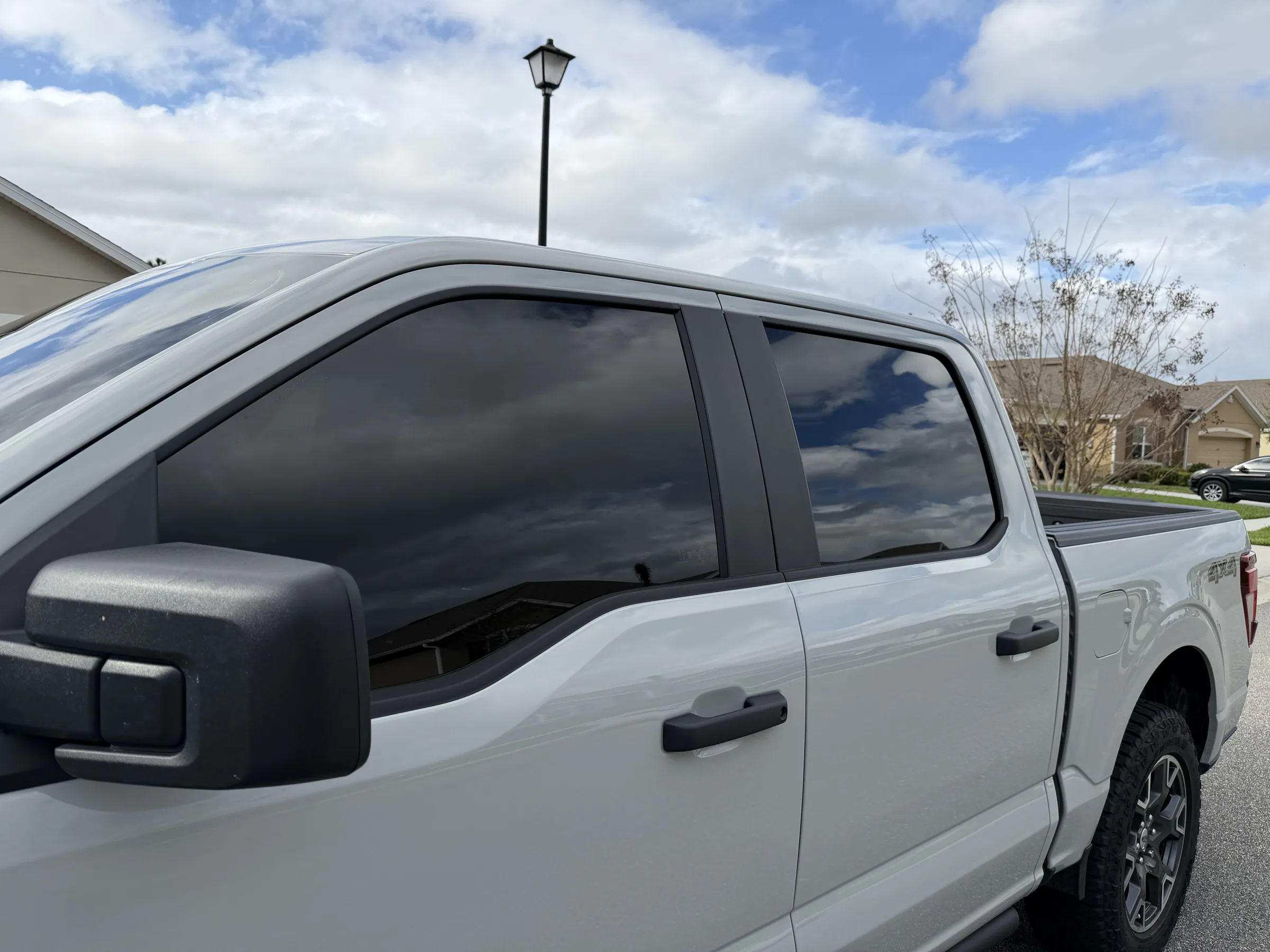 A white pickup truck with dark window tint applied to the cab windows, parked in a residential driveway.