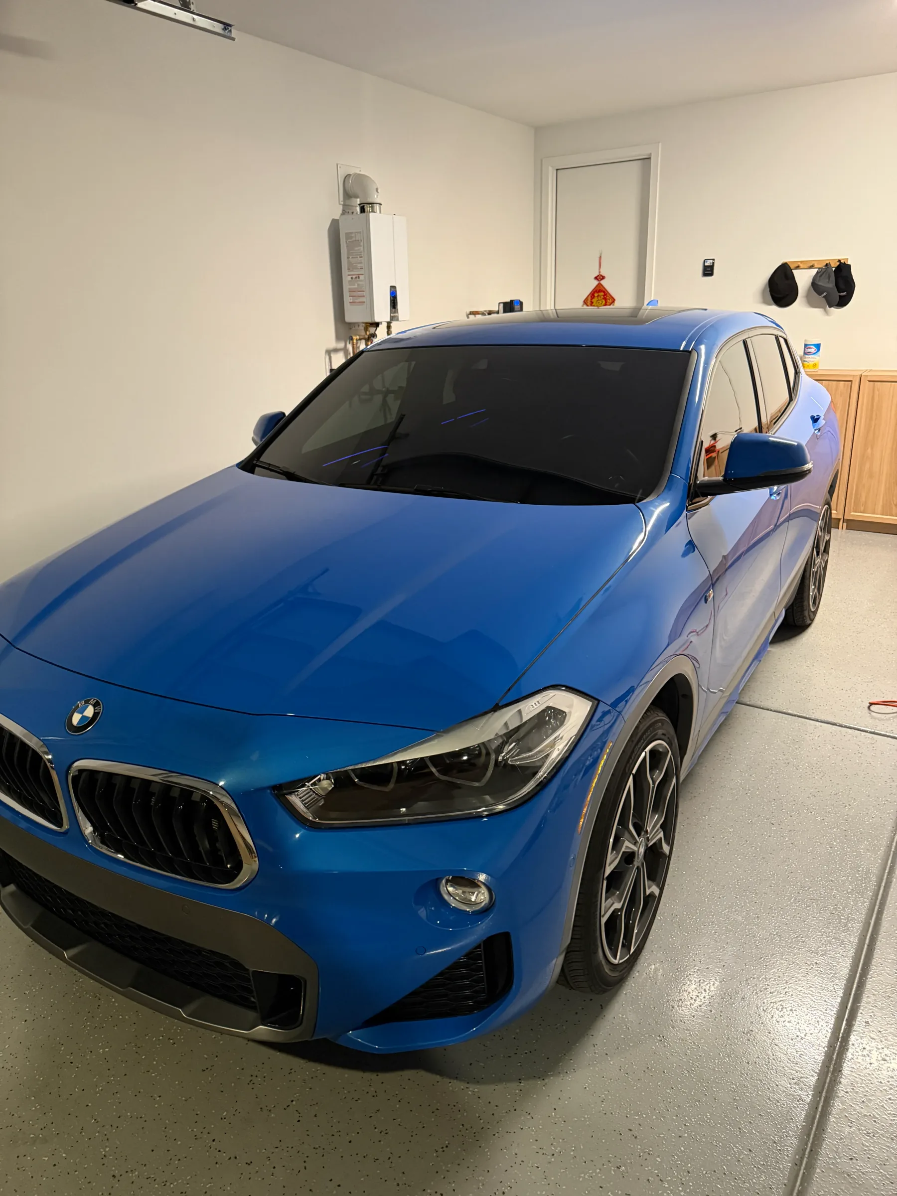 Blue BMW X2 with dark window tinting applied, parked indoors during service at a tinting facility.