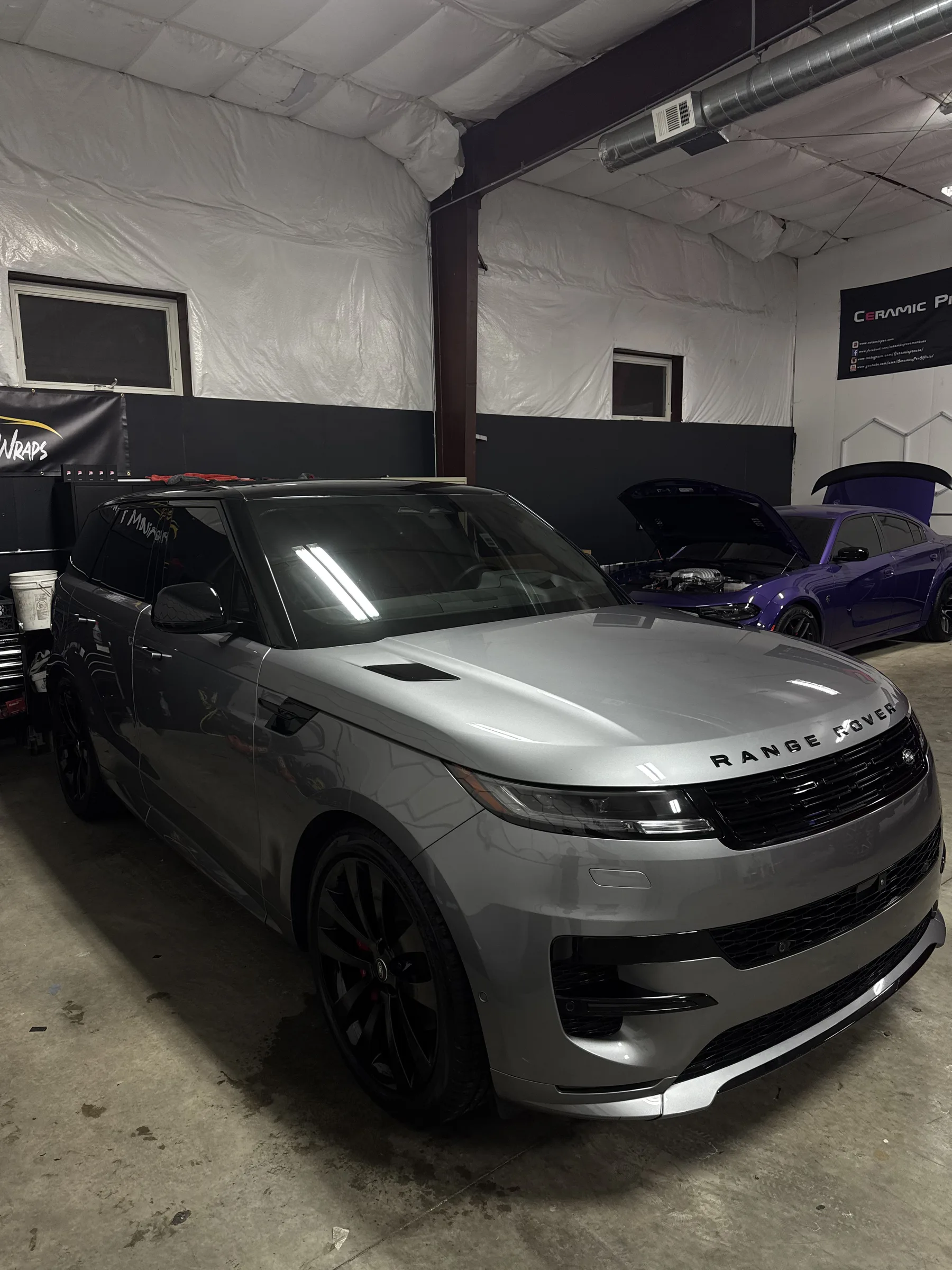 White Range Rover in an automotive shop receiving paint protection film installation, displayed in a climate-controlled garage with other vehicles in the background.
