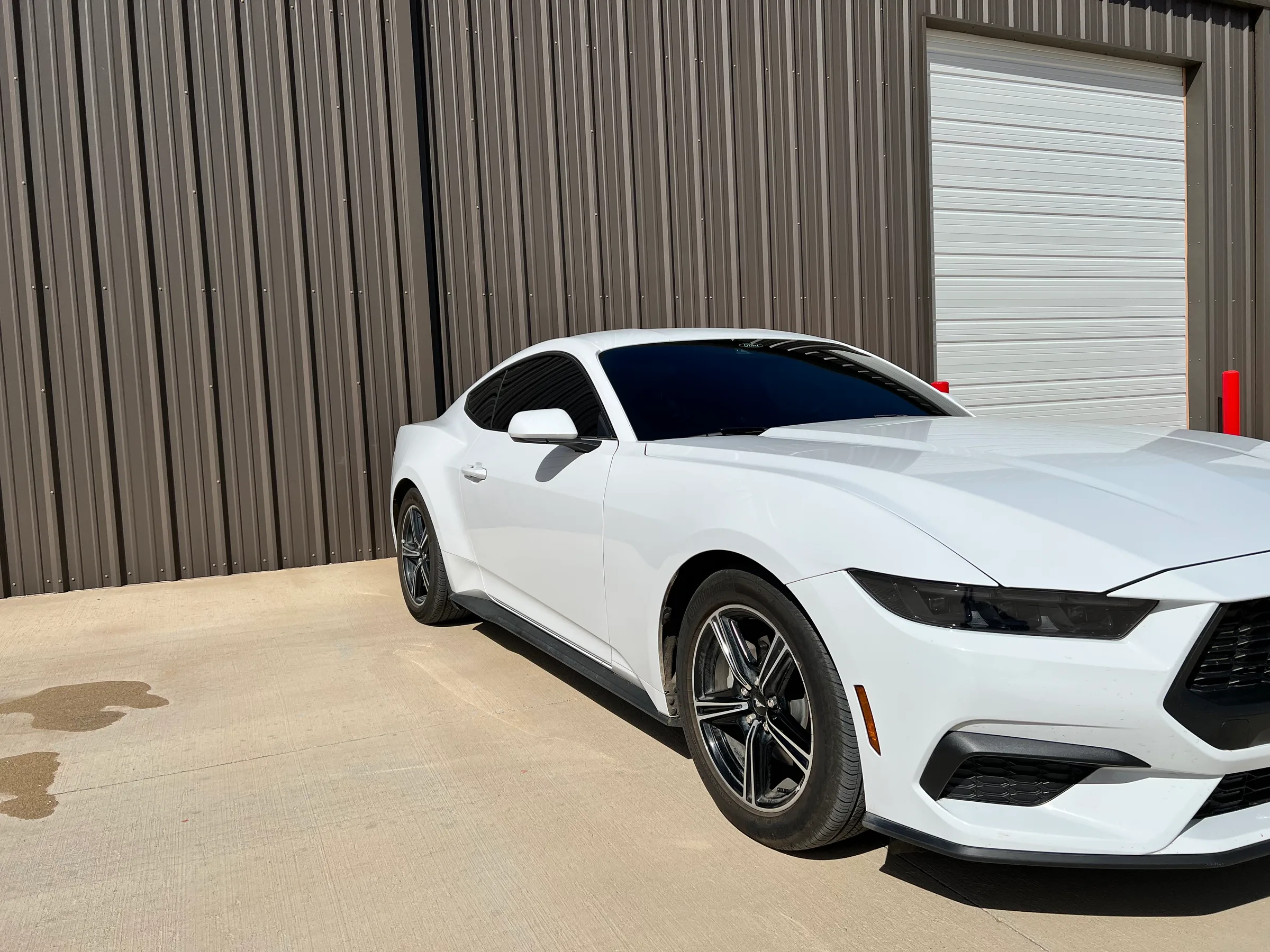 A white Ford Mustang with darkly tinted windows parked in front of a metal garage building.