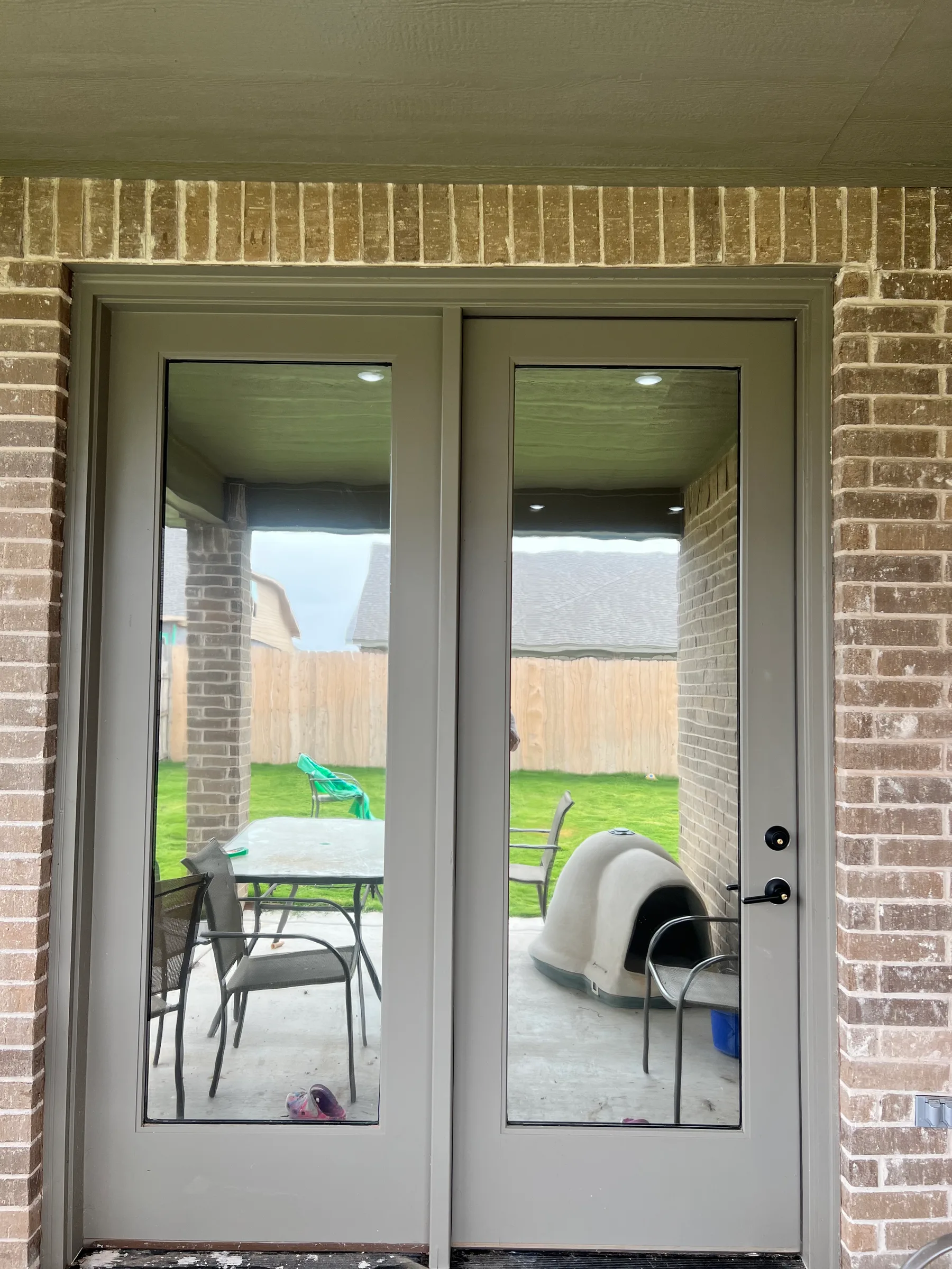 A pair of glass back doors with window tint applied, looking out onto a backyard patio with furniture and fencing.