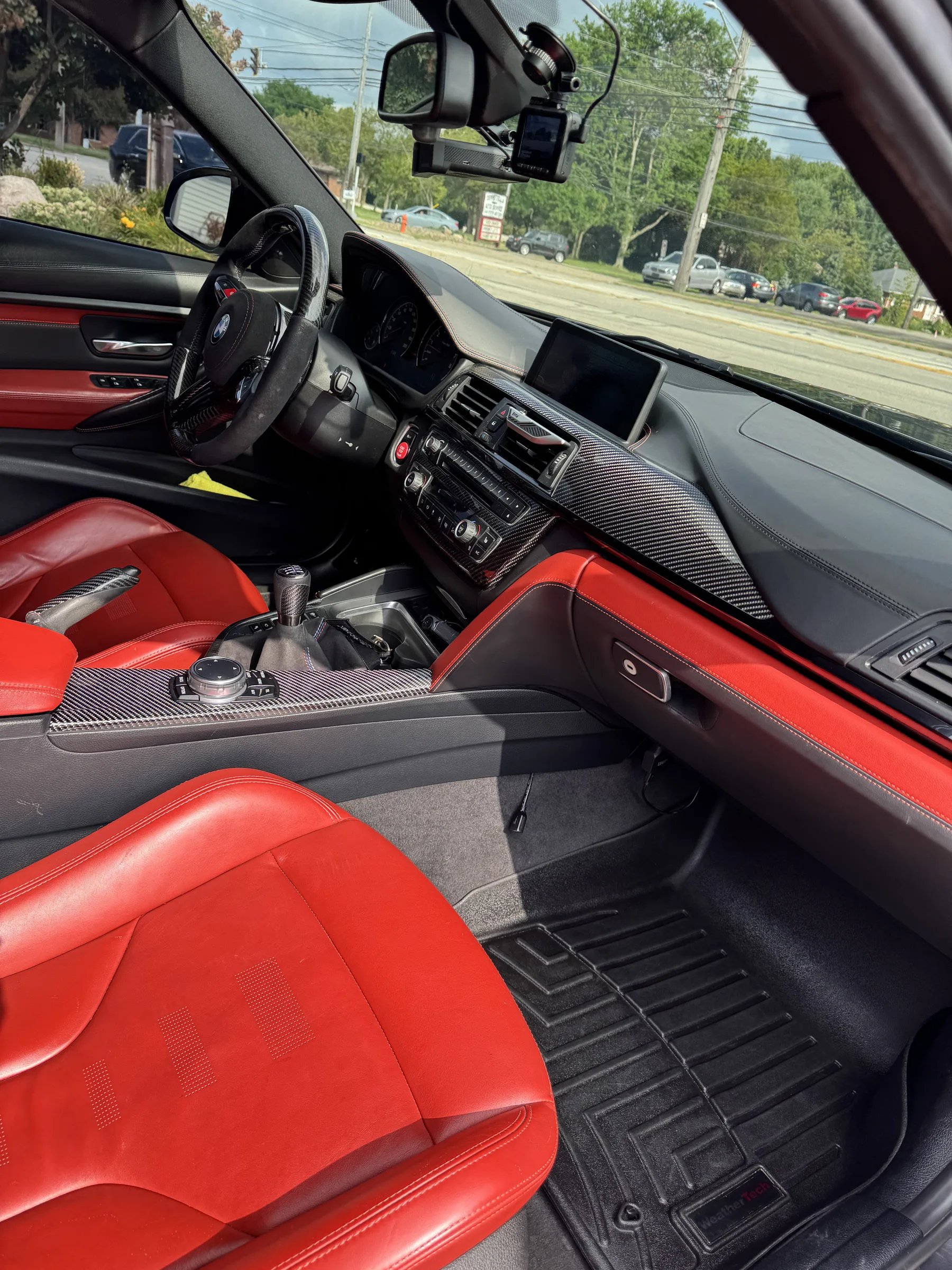 Interior view of a red and black BMW M Sport showing dashboard with carbon fiber trim, red leather seats, and tinted windows while parked on a road in Berea, Ohio.