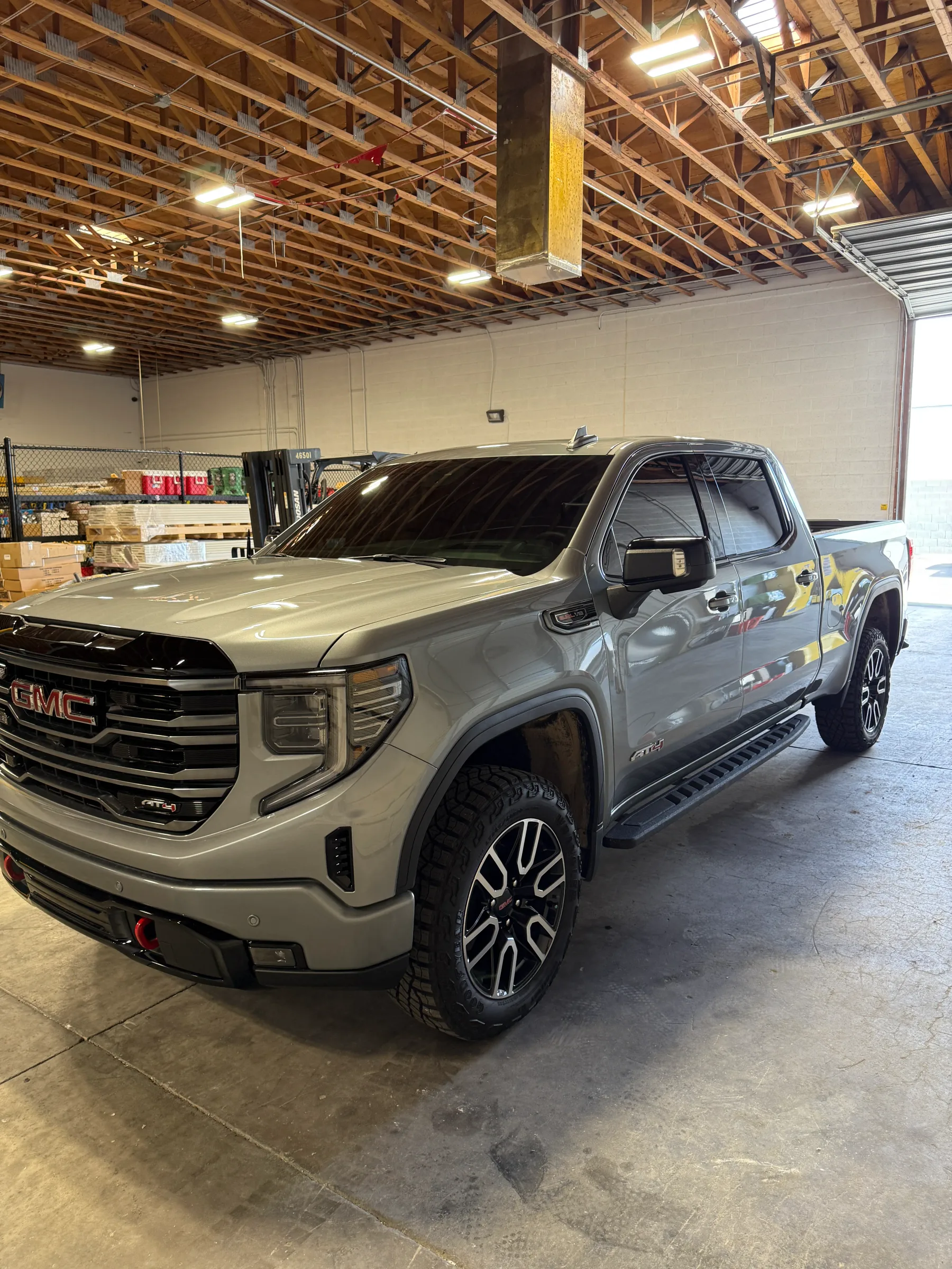 A pearl-white GMC Sierra pickup truck with dark window tinting applied to all side and rear windows, displayed in an indoor shop facility.