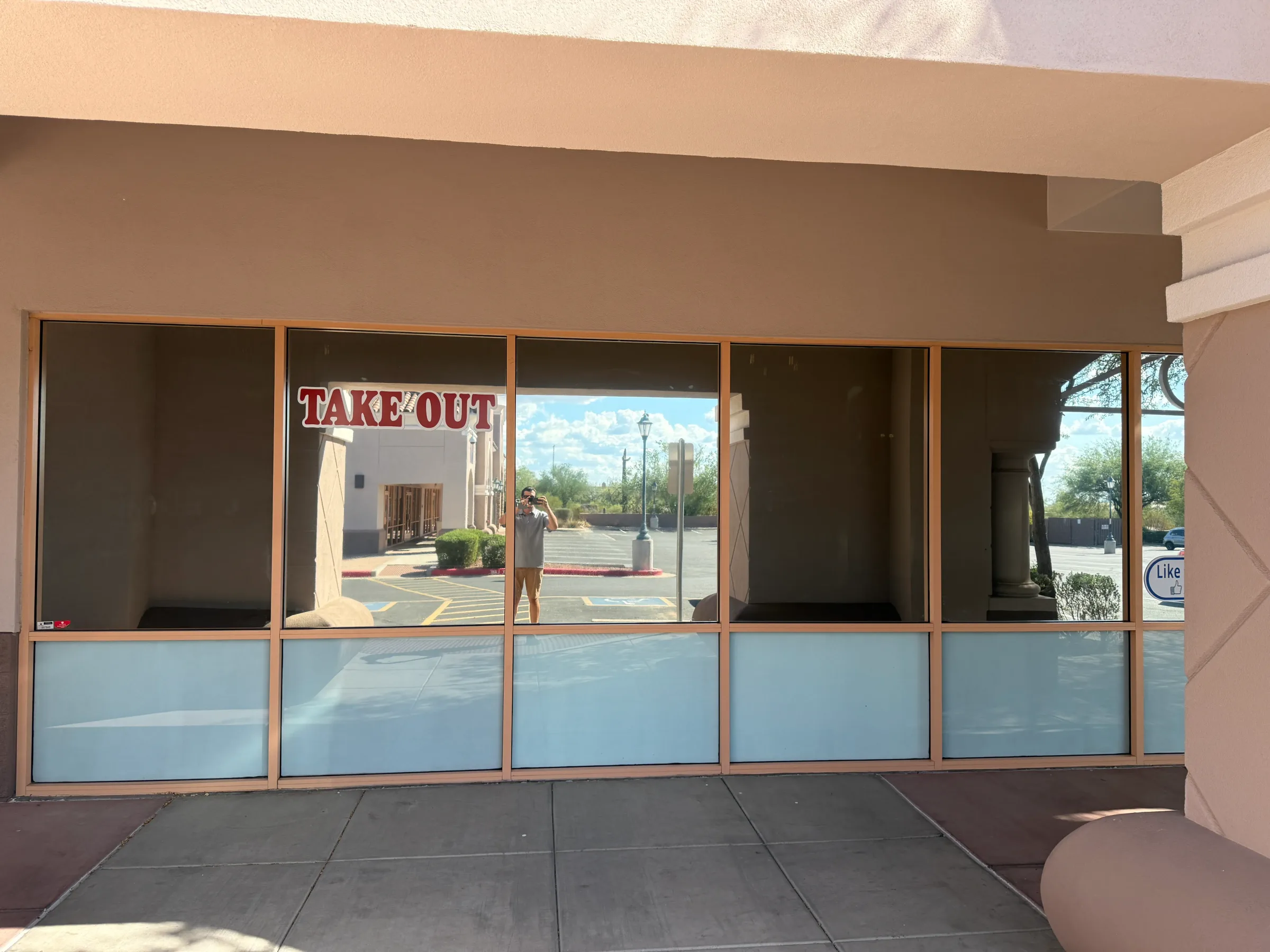 A commercial storefront with large windows featuring a blue tint on the lower glass panes and darker tint on the upper sections, with a "TAKE OUT" sign visible inside.