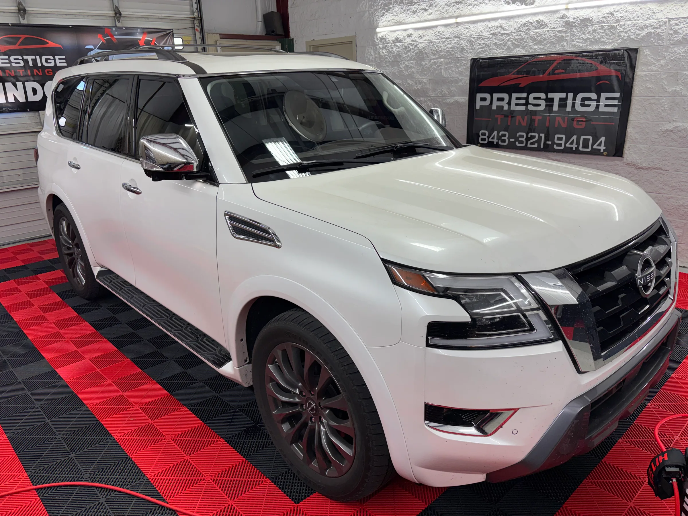 White Nissan Armada SUV with dark window tint displayed in a shop showroom with Prestige Tinting signage.