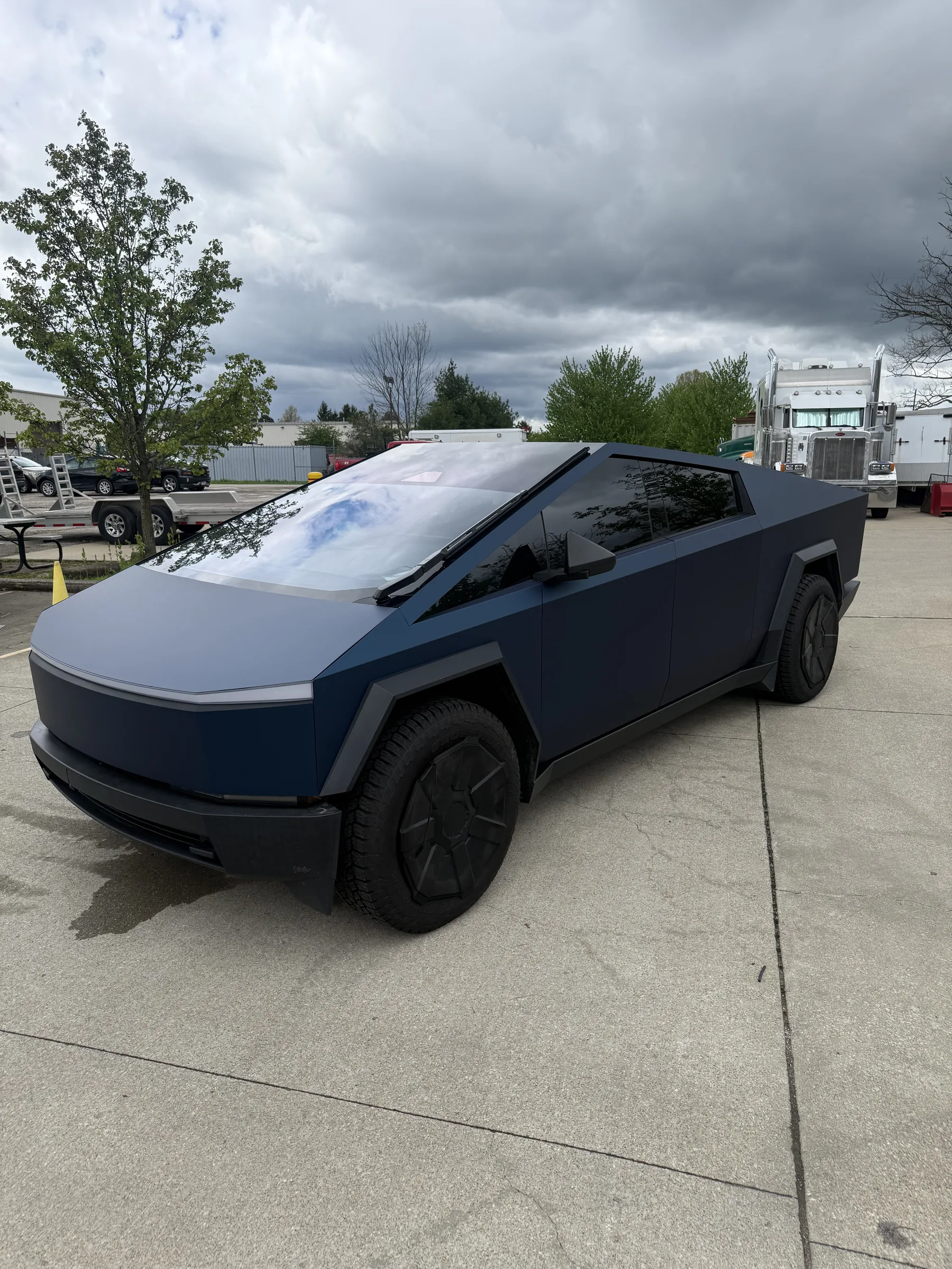 A Tesla Cybertruck with a two-tone vinyl wrap featuring a dark blue lower half and light gray upper half, displayed in a commercial lot in Berea, Ohio.